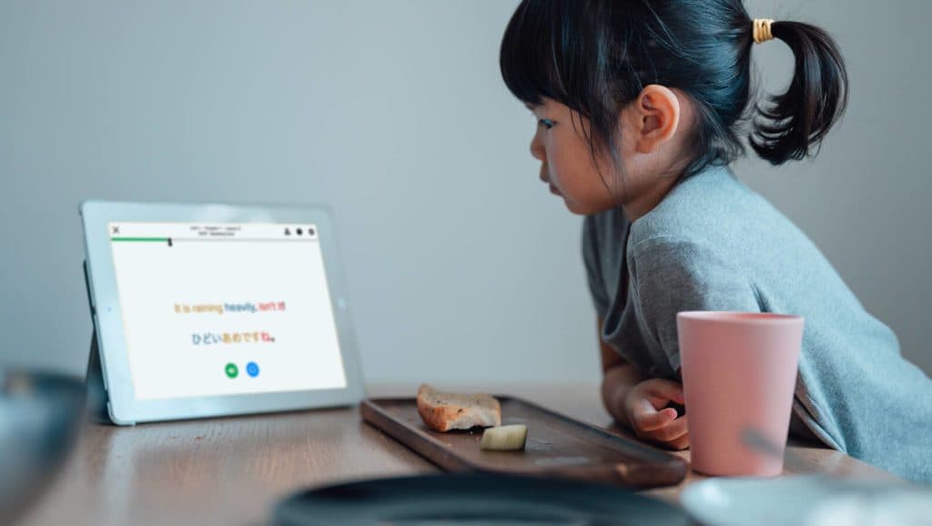 A young girl sitting at a table with a tablet doing a Mango lesson