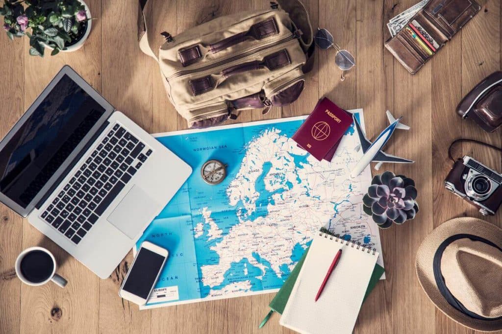 A table with a backpack, a wallet, a camera, a hat, a map and open laptop spread across it