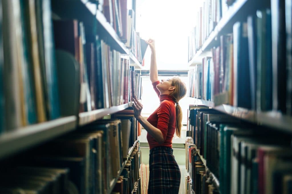 A young girl looking through books among crowded shelves