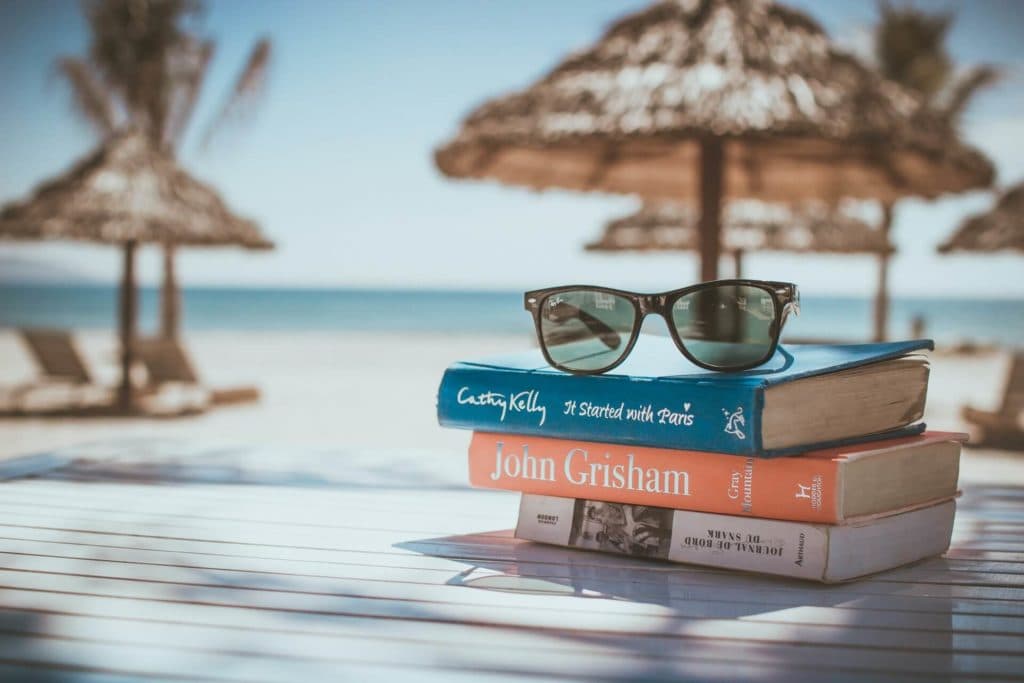 3 books on a table at the beach with a pair of sunglasses sitting on them