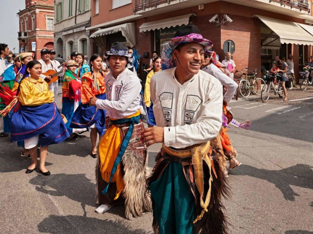 Hispanic people wearing traditional clothes dancing down the street