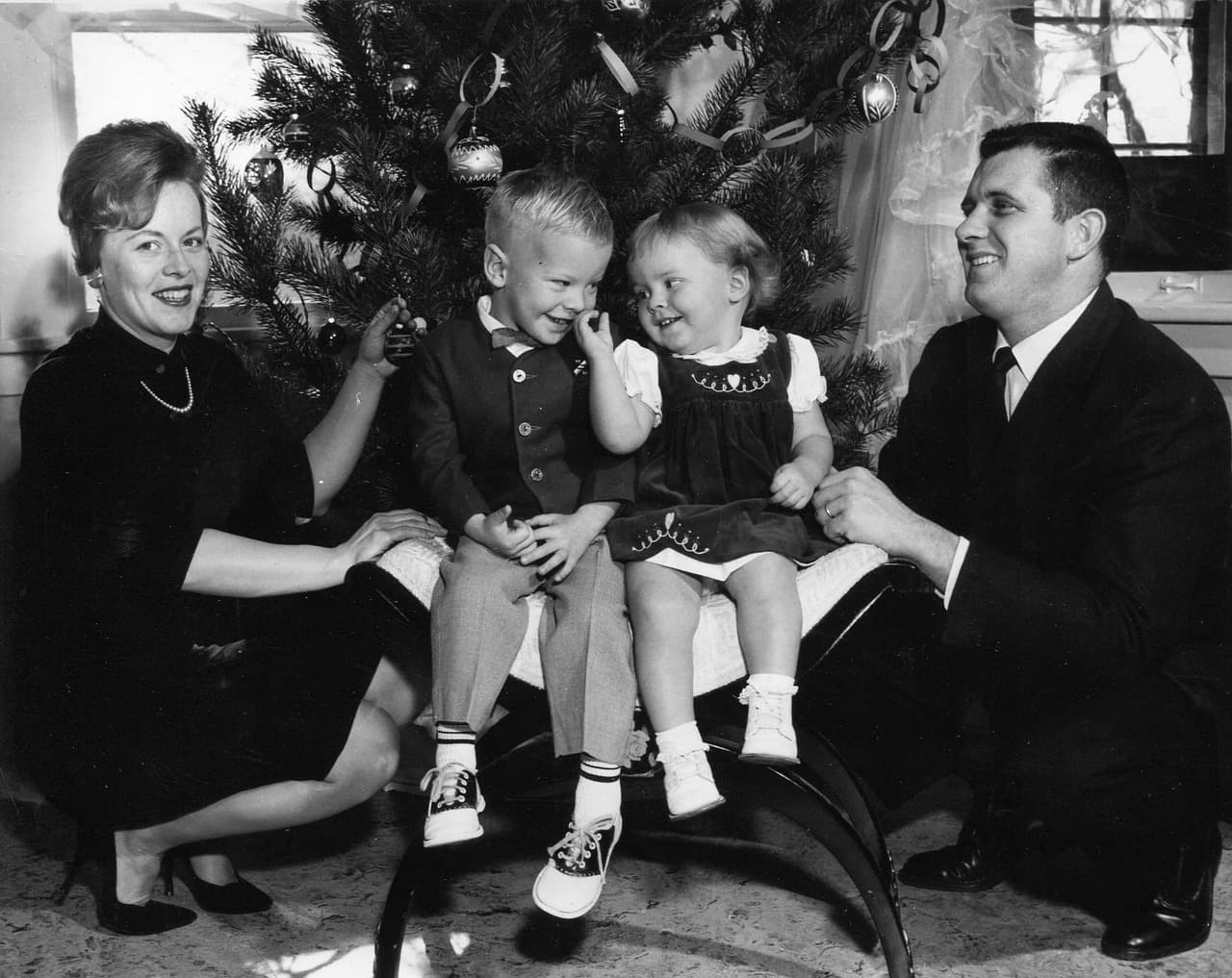 An old black-and-white photo of a family in front of a Christmas tree. A mother, father, and a little boy and girl.