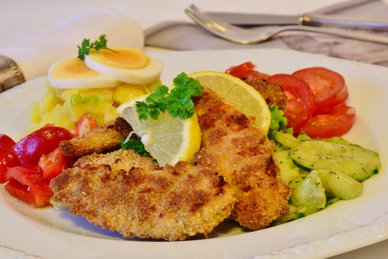 A photo of a plate of schnitzel with lemons on top and egg salad and other vegetables on the side.