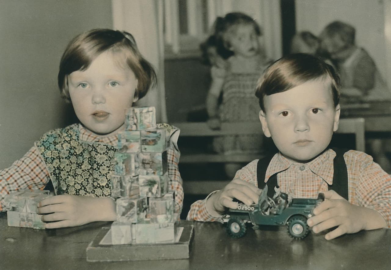 An old black-and-white photo of a boy and girl sitting at a table with some toys.