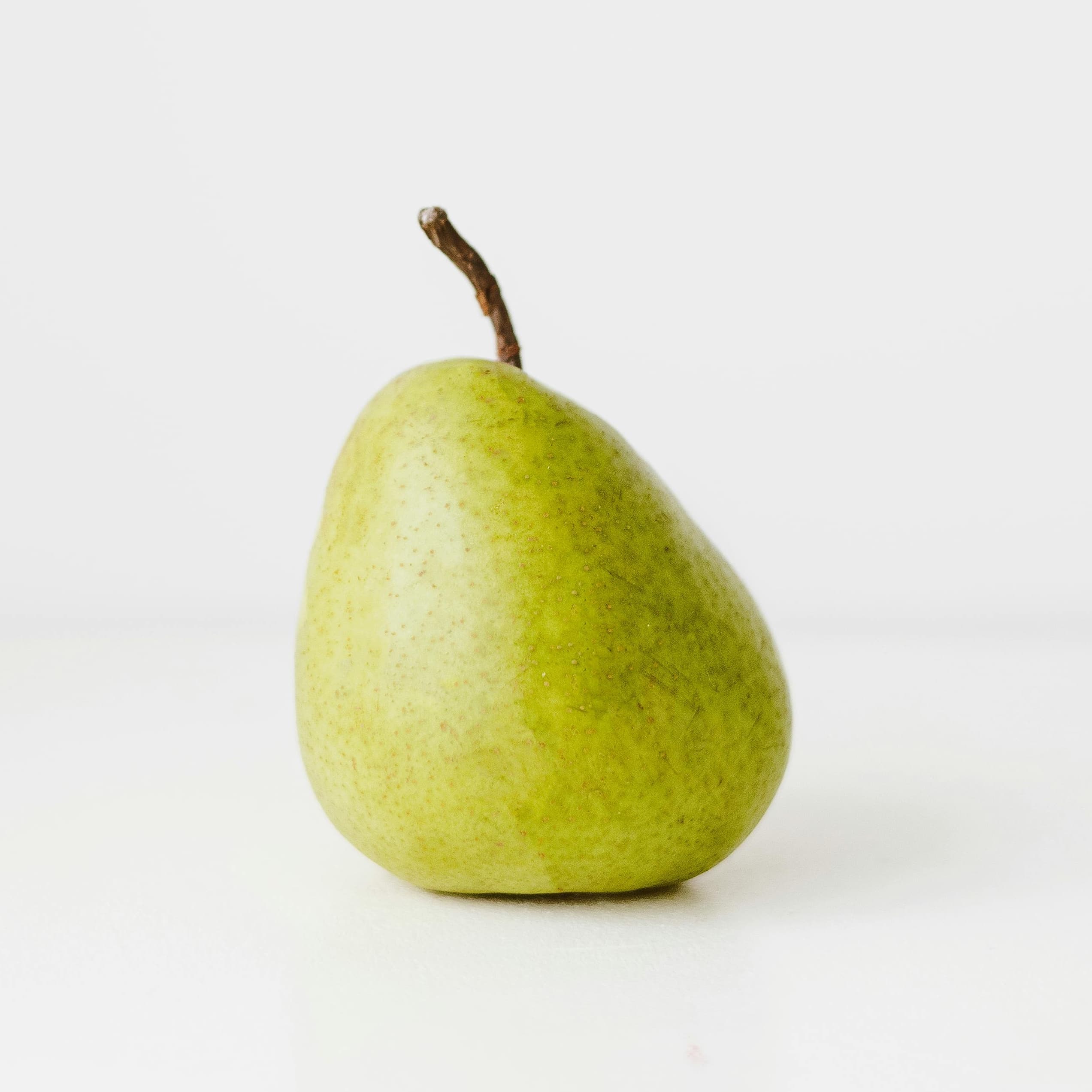 A photograph of a small green pear on a white background.