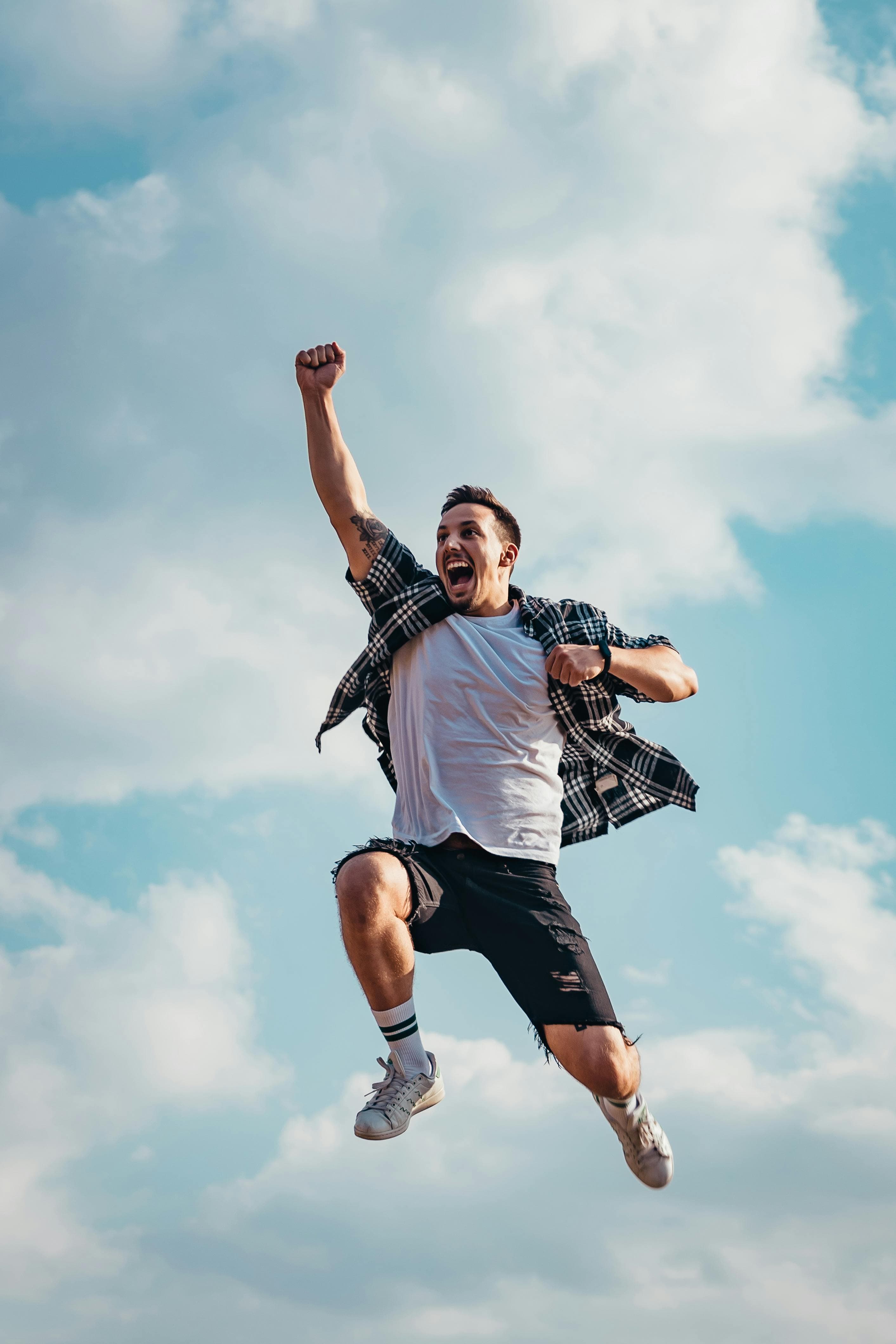 A photo of a young man in casual clothes jumping high into the air and cheering.