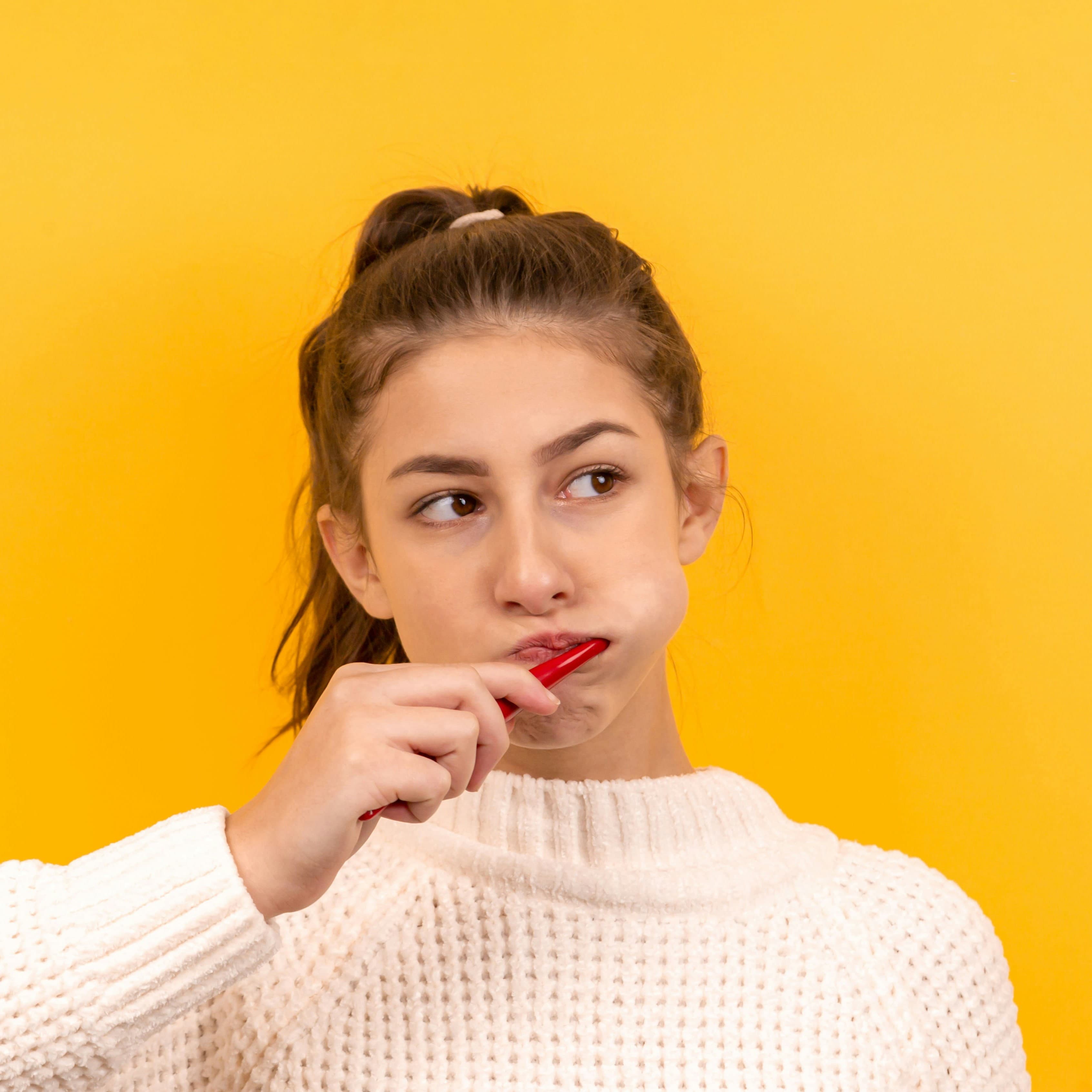 A woman brushing her teeth in front of a yellow background.