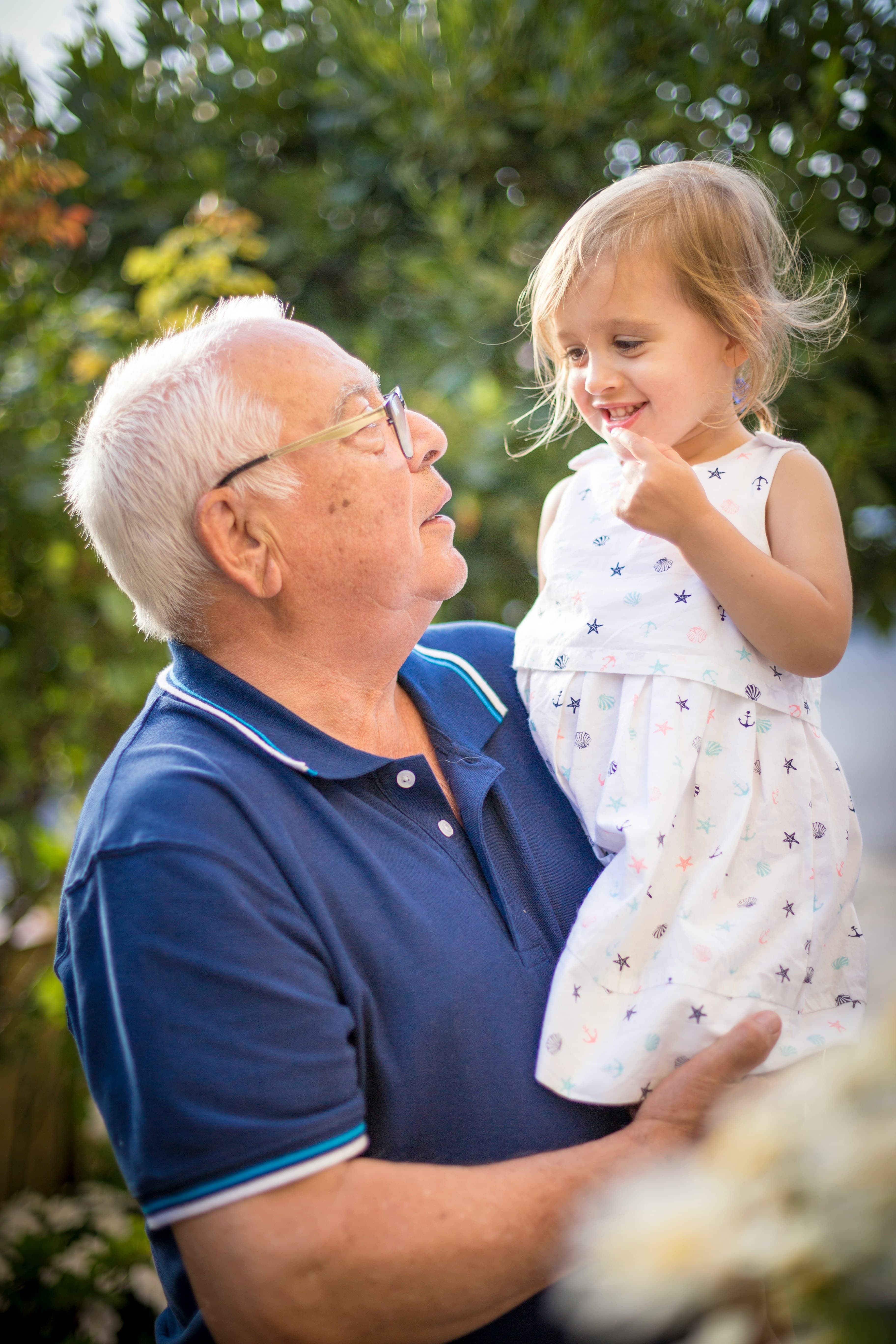 A grandfather is holding his granddaughter, a girl who is about 3-4 years old.