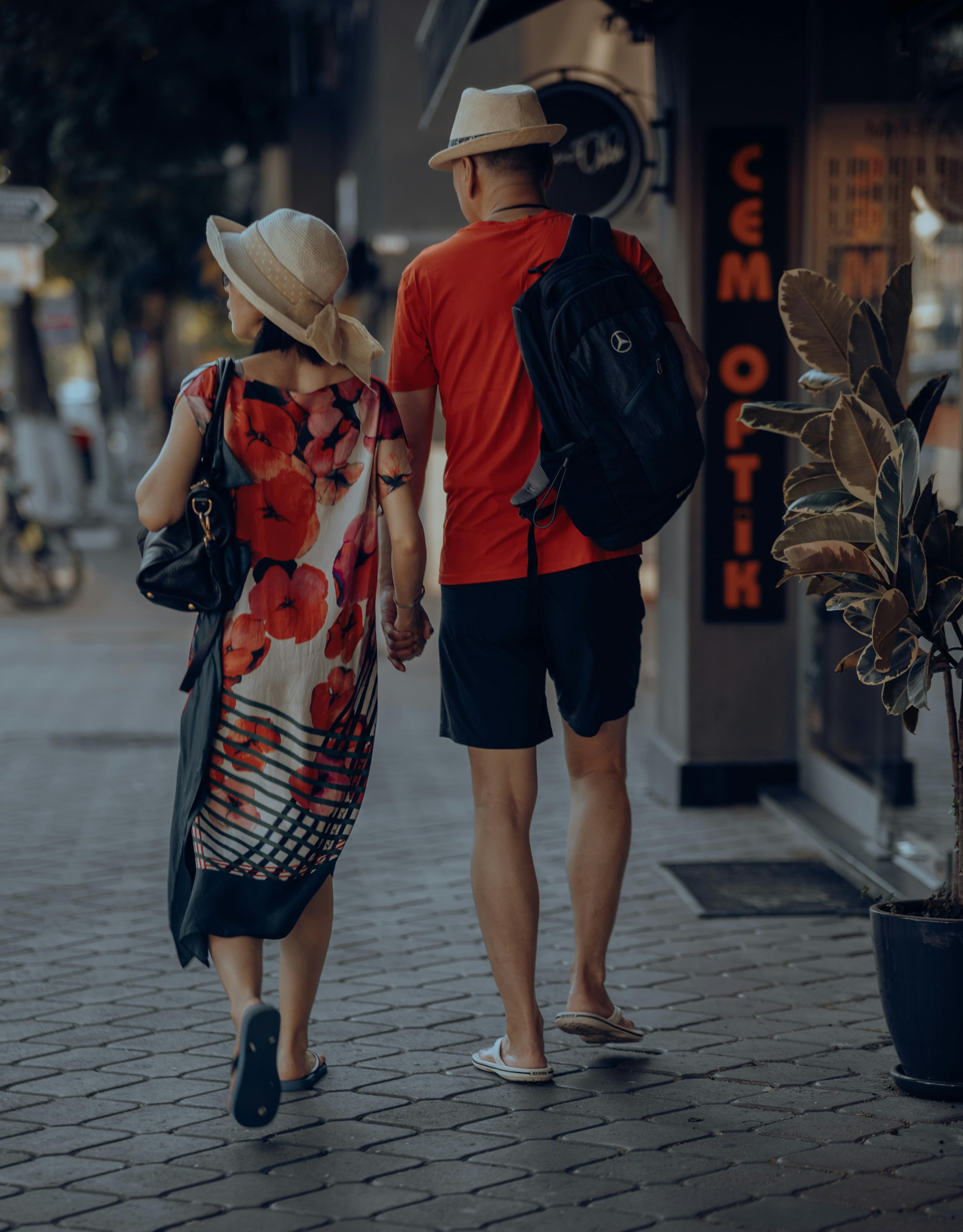 A photo a man and a woman dressed like tourists, walking down a street in summer clothing. The photo is taken from behind.