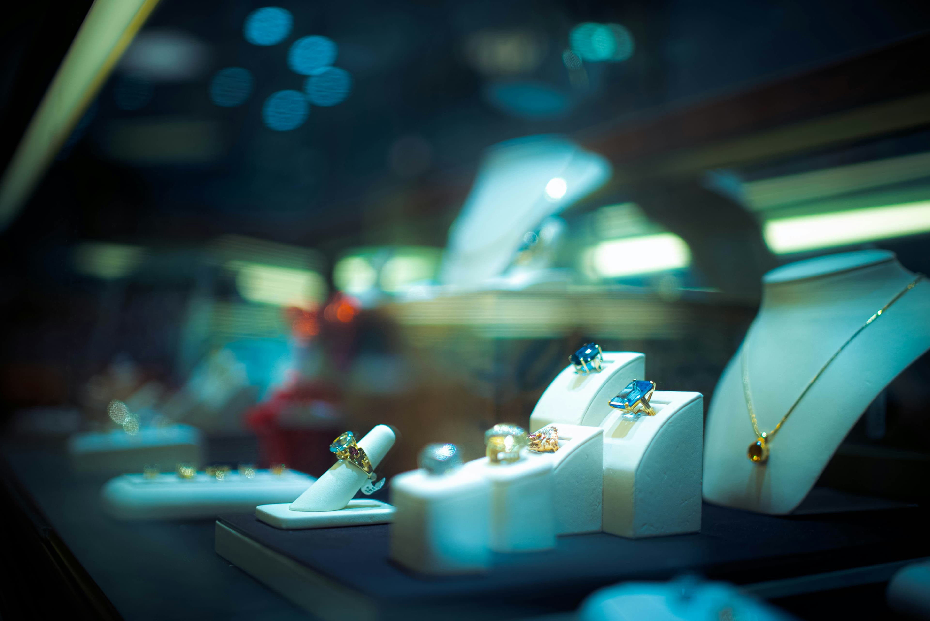 A photo of a display case at a jewelry store. Mostly we can see several jeweled rings and one necklace.
