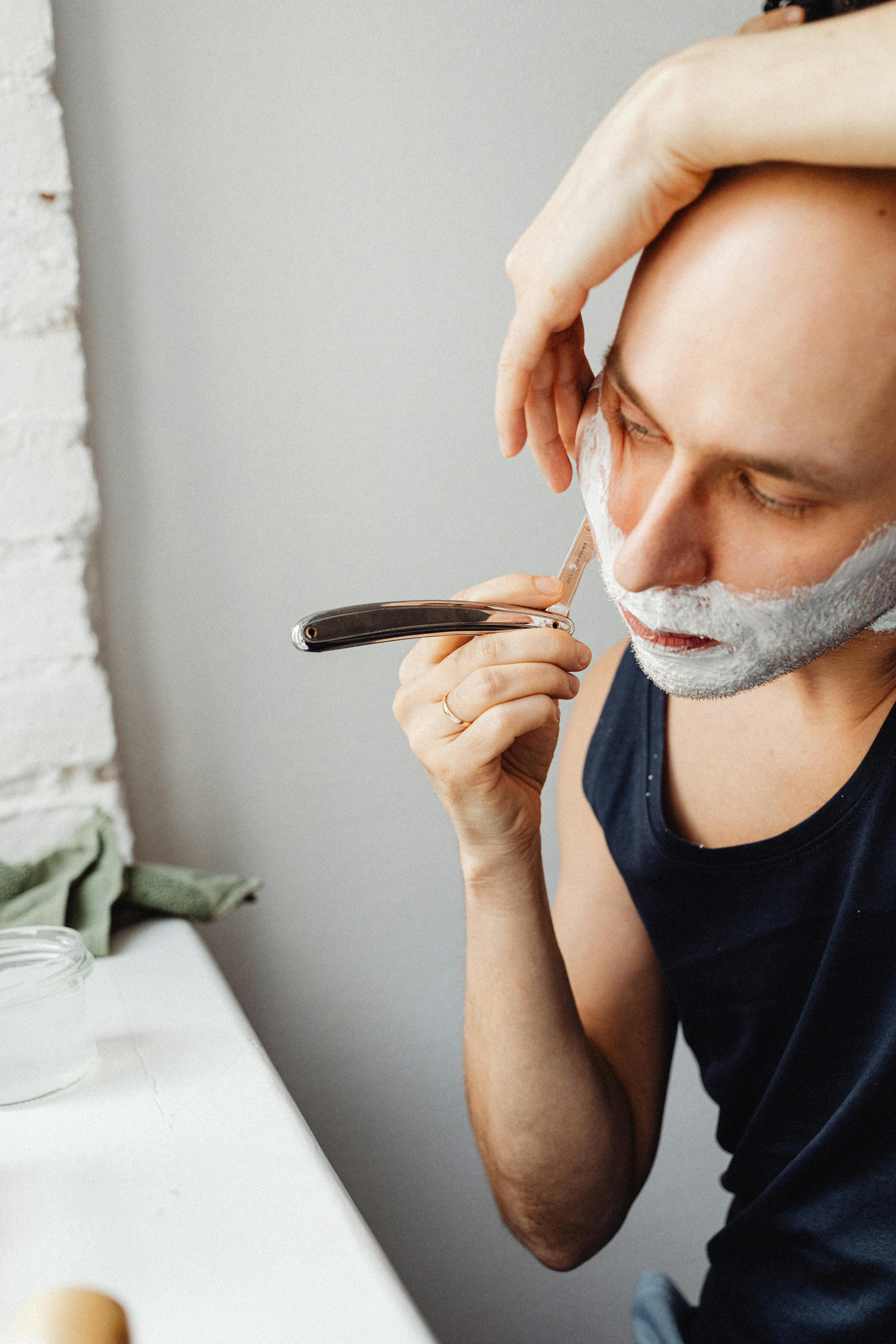 A photo of a man shaving his face with a straight razor.