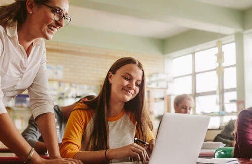 A teacher helping a student working on her laptop