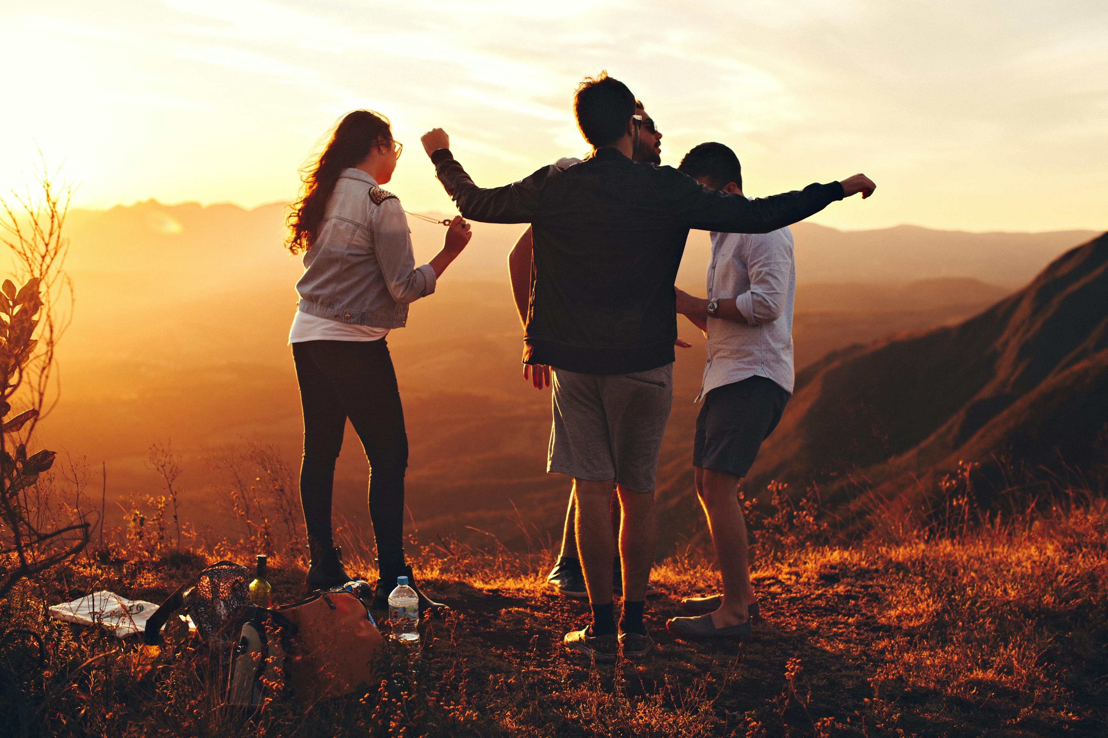 A photo of a group of four young people hanging out on a mountainside at sunset.