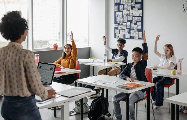 A teacher with four students all with their hand raised, ready to answer a question