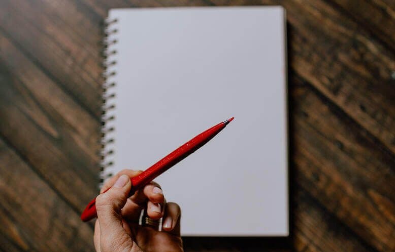 A blank notebook and a person holding a red pen reading to write on it