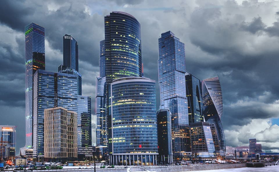 A photo of tall modern buildings in front of storm clouds. Some of the lights are on inside the towers.