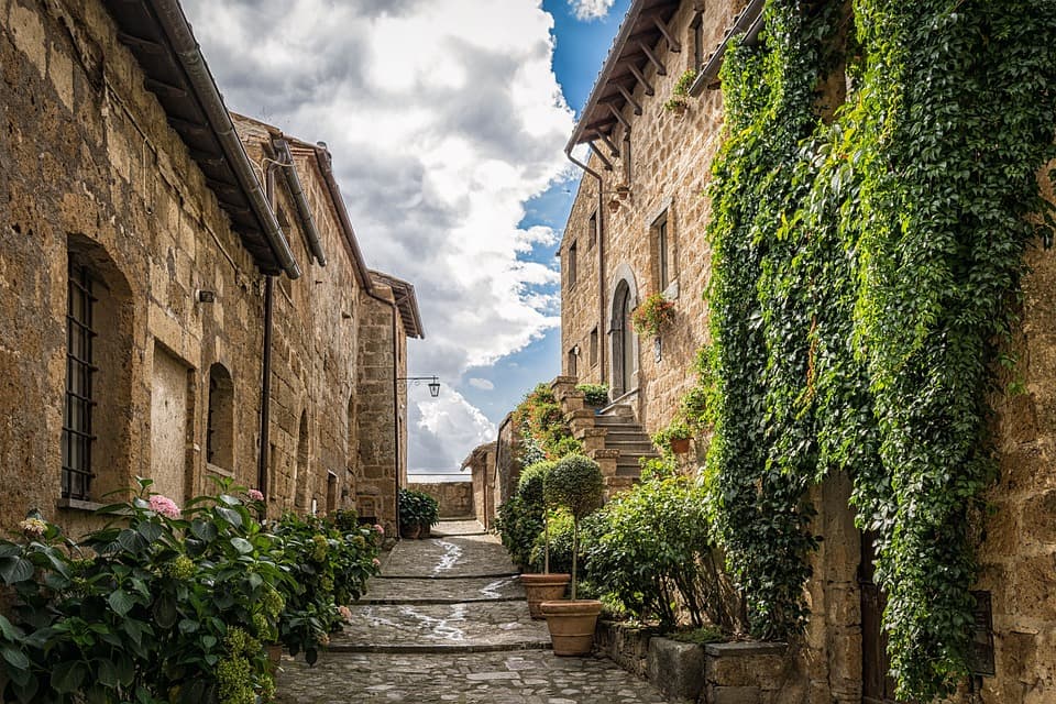 A photo of an alley between ancient stone walls. We are looking at a small house at the close end of the row.