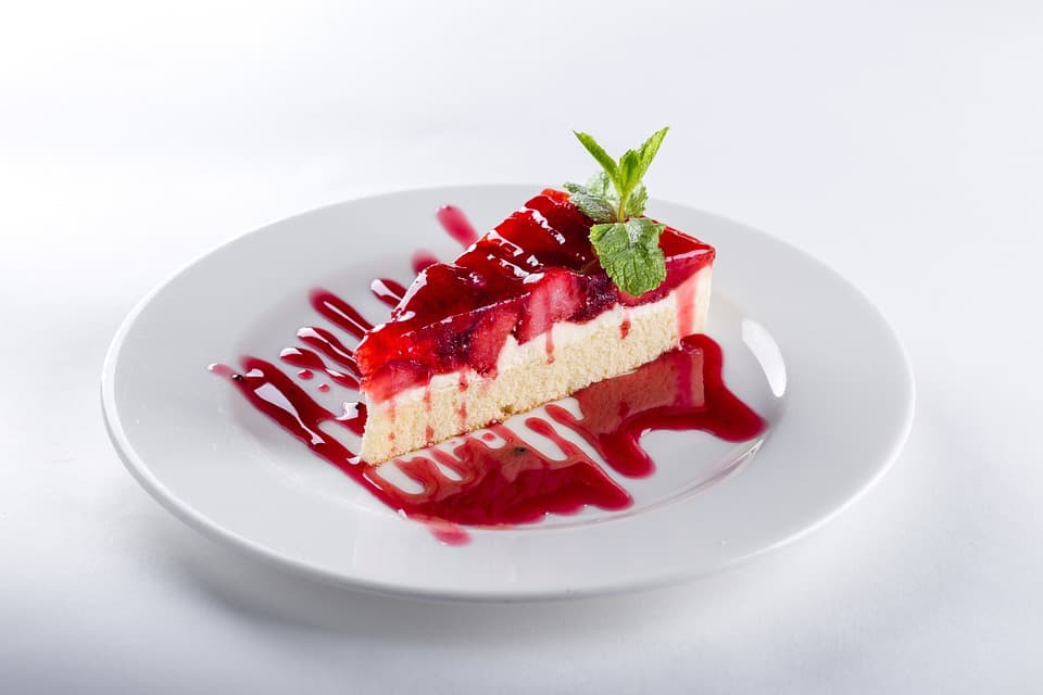 A photo of a slice of white cake topped with strawberries, strawberry sauce, and a sprig of mint.
