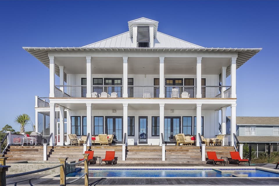 A photo of a very large white house with a two story porch and a pool.