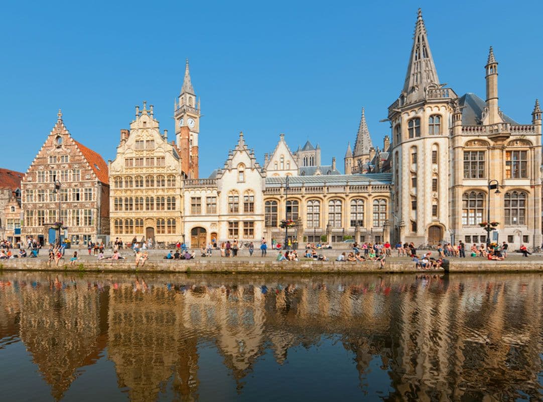 In Belgium, ornate guild houses face a busy walking trail along a river.