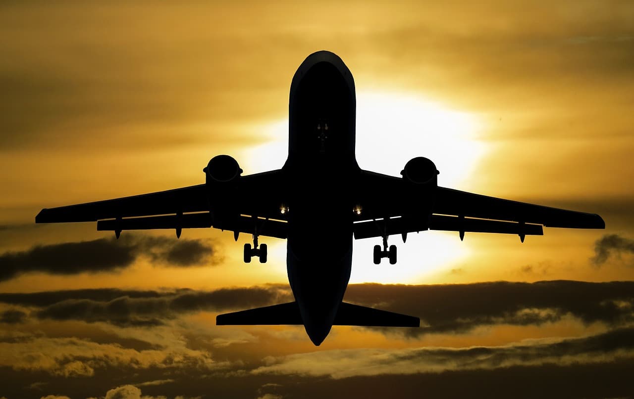 A photo of a an airplane taking off, silhouetted against the sun.