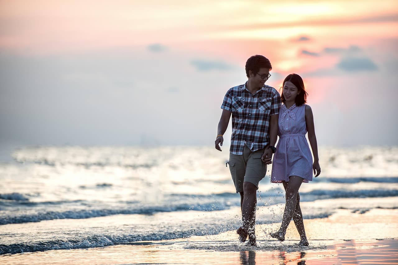 A photo of a couple walking down the beach at sunset.