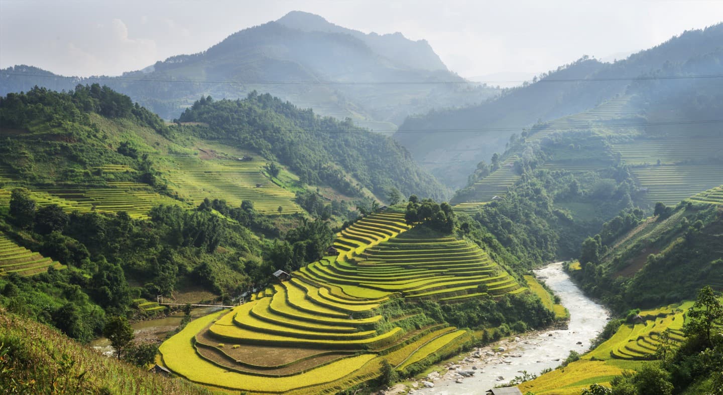 An aerial shot of forested mountains in Vietnam. A river runs around grassy green steppes.