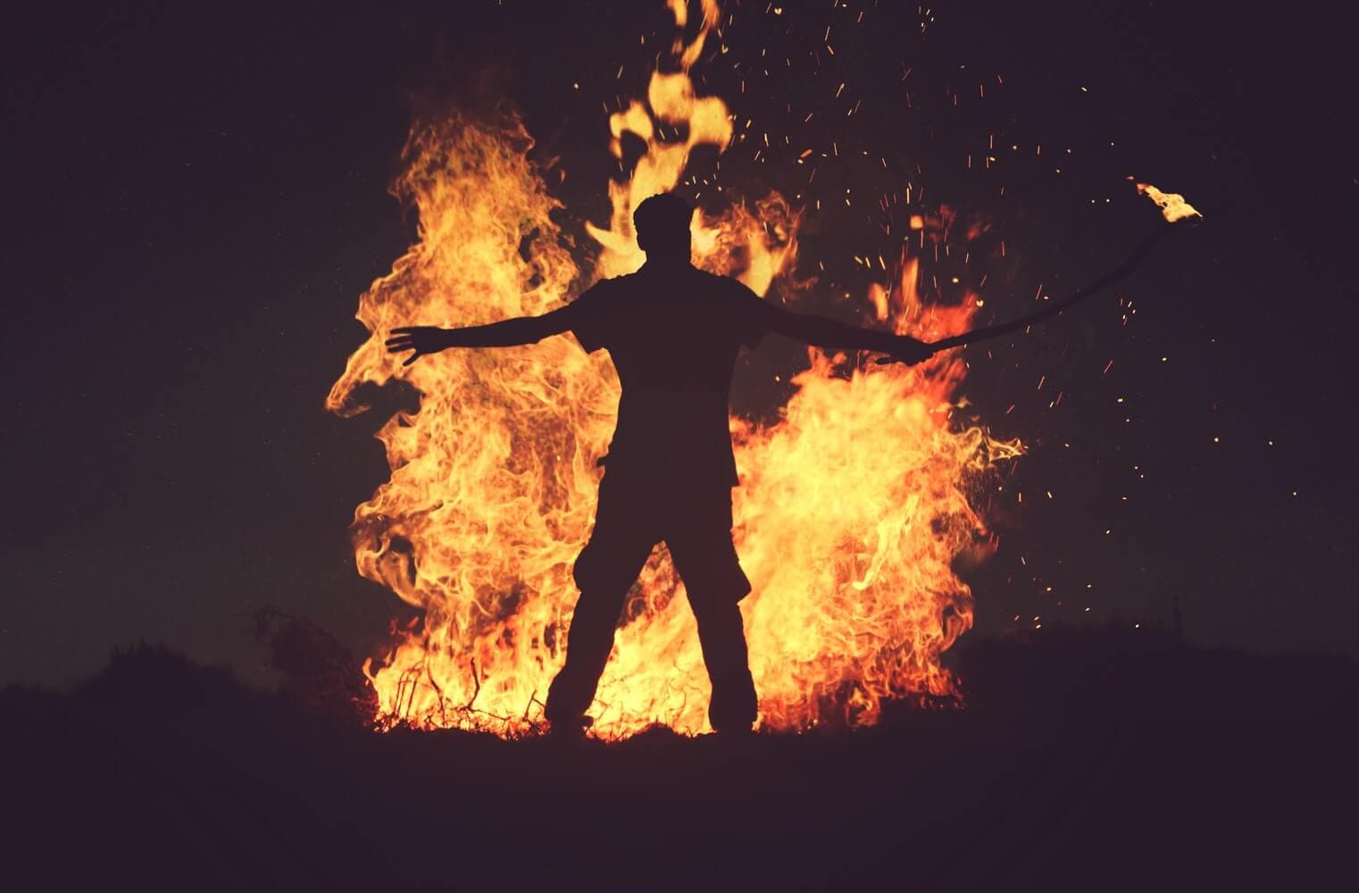 A man lighting up a big bonfire at sunset