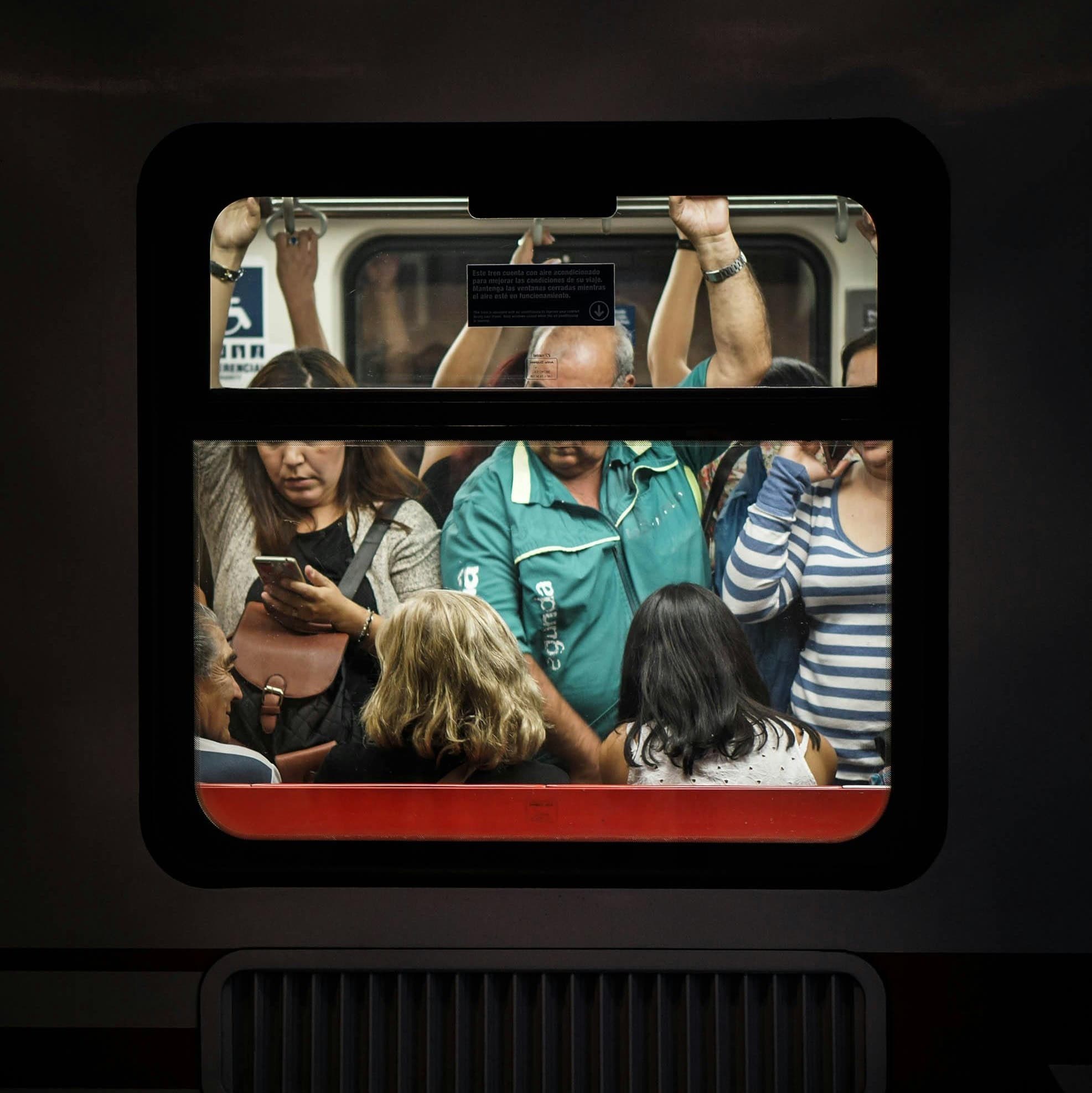 A photo of a train car taken from outside the window. There are a lot of people on the train.