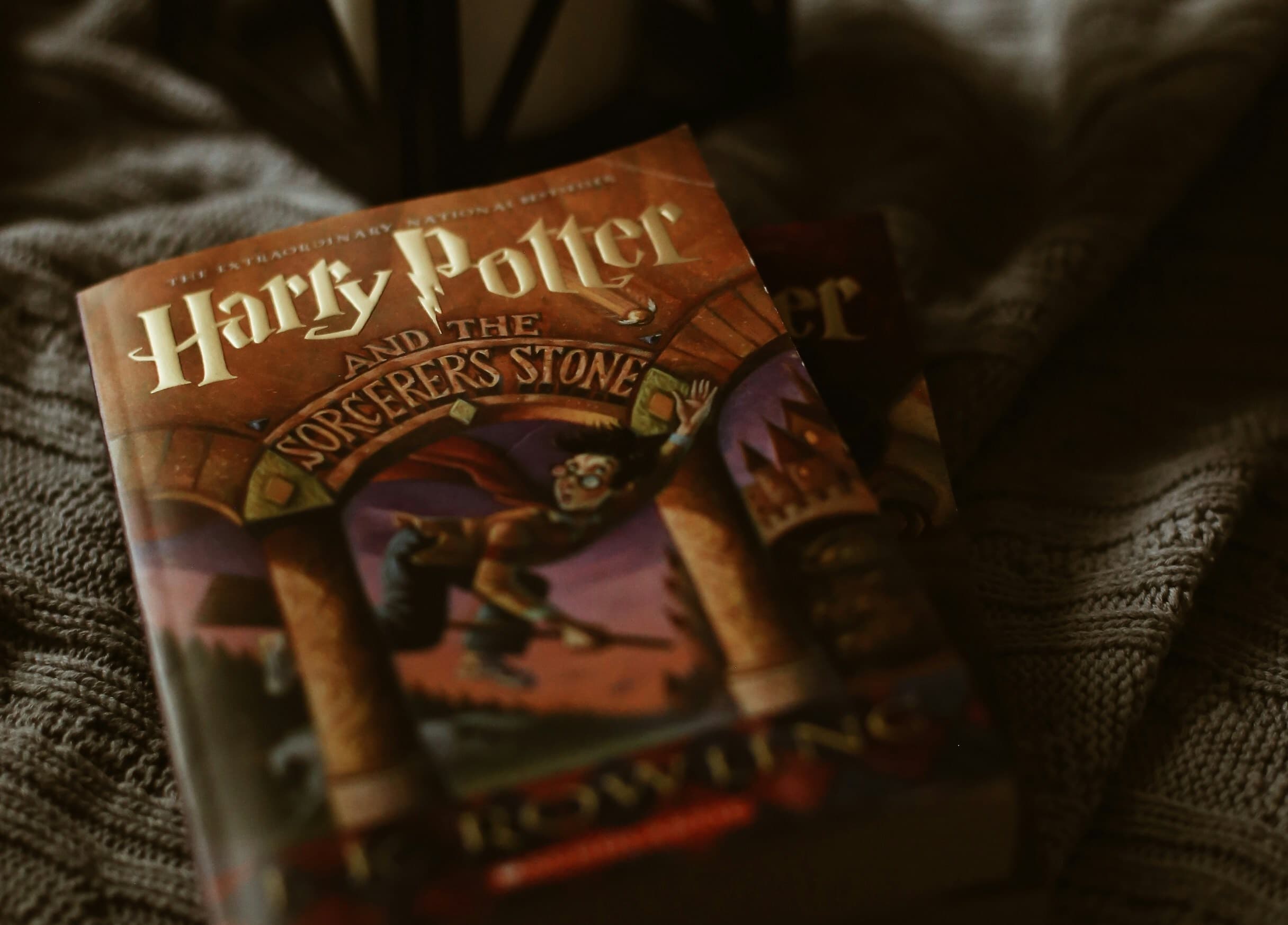 A copy of Harry Potter and the Sorcerer's Stone is lying on a gray blanket.