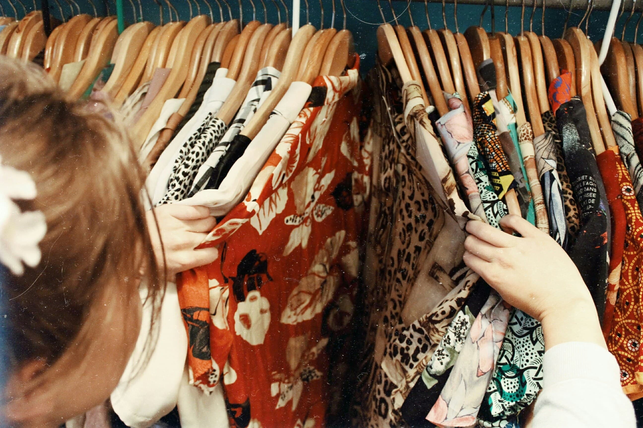A photo of a woman looking through a bunch of bright-colored dresses on hangers.