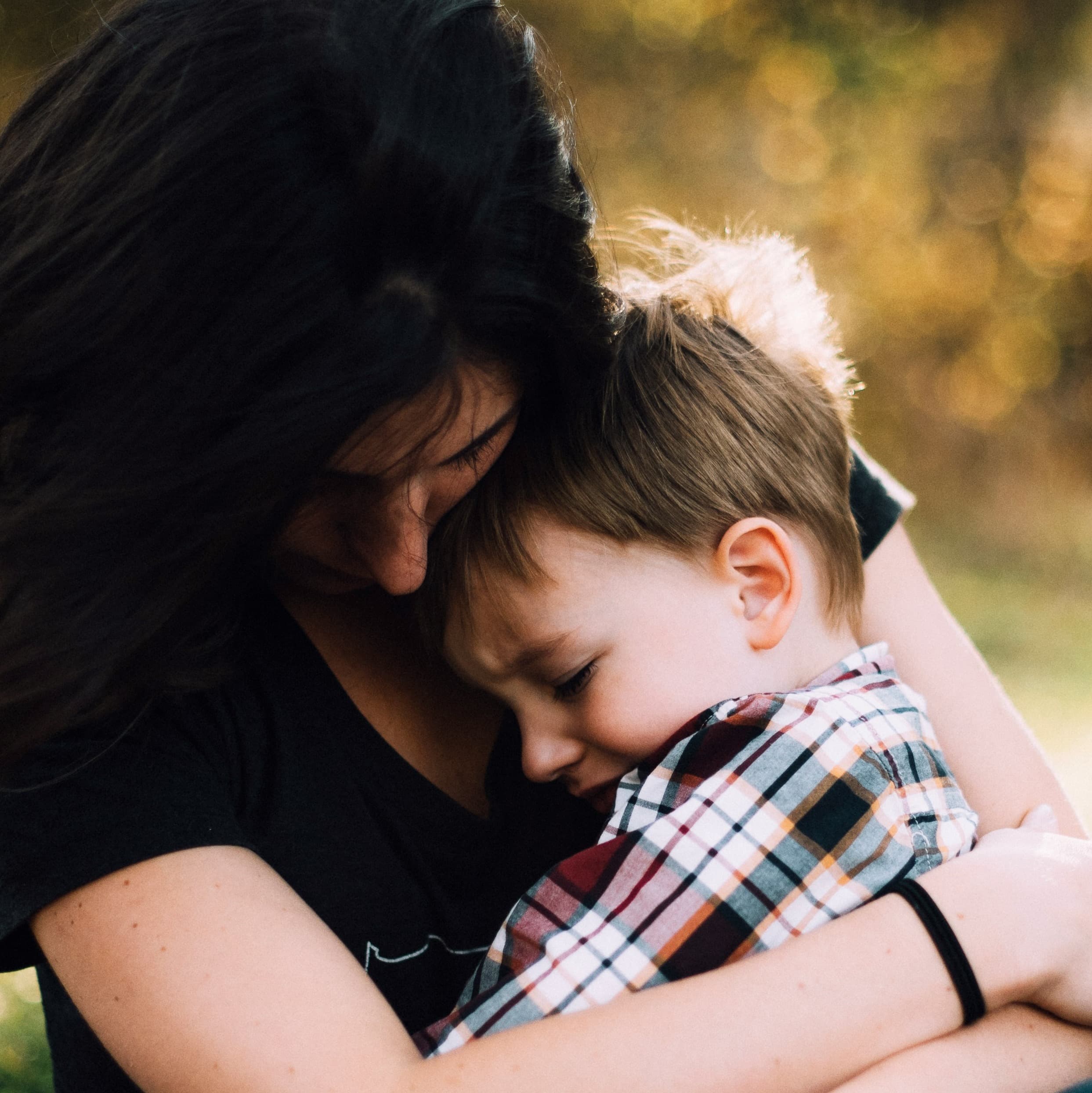 A smaller version of the picture above: a woman with dark hair holds a young blond boy on her lap and hugs him as he cries