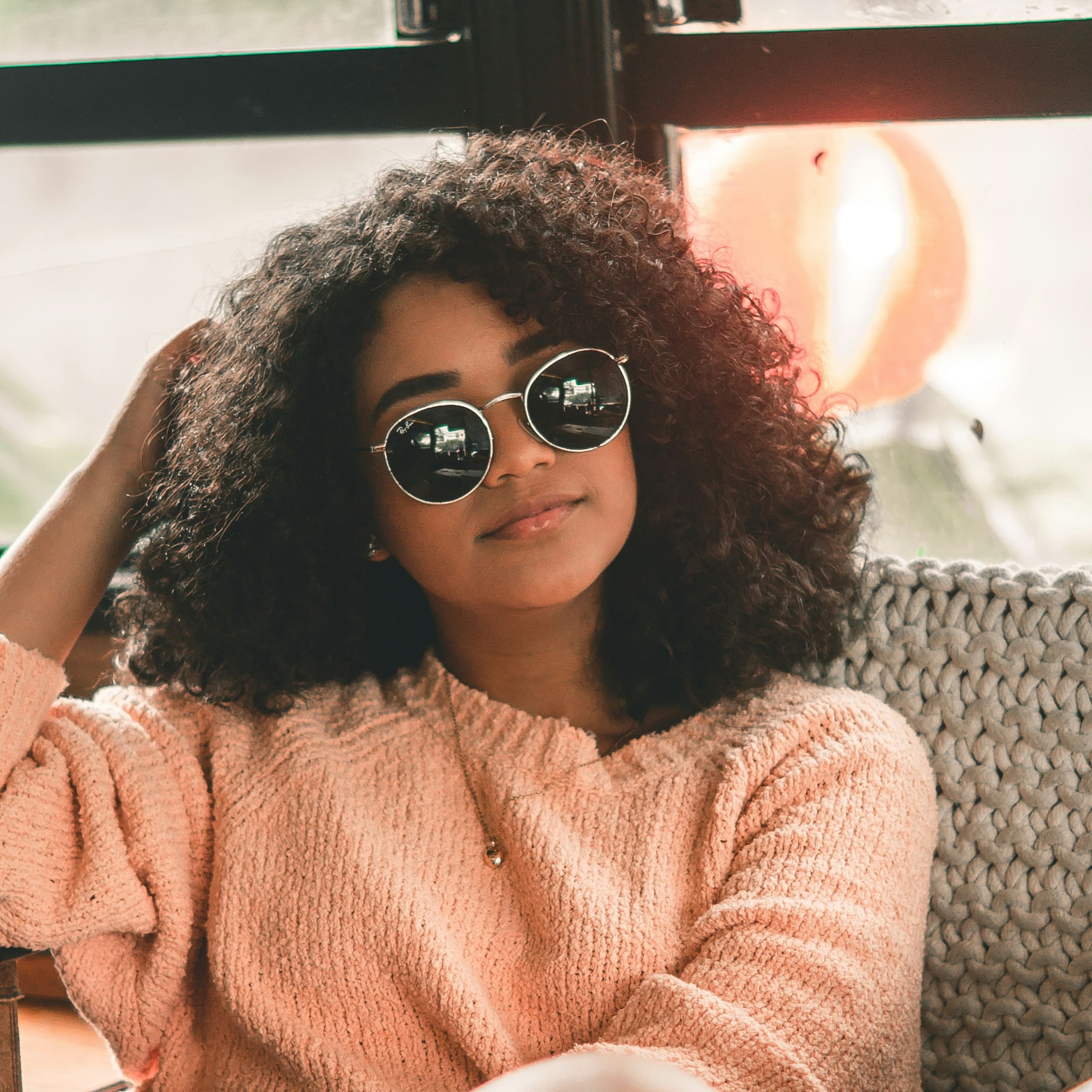 A photo of a young woman with brown skin, sunglasses, and very curly hair.