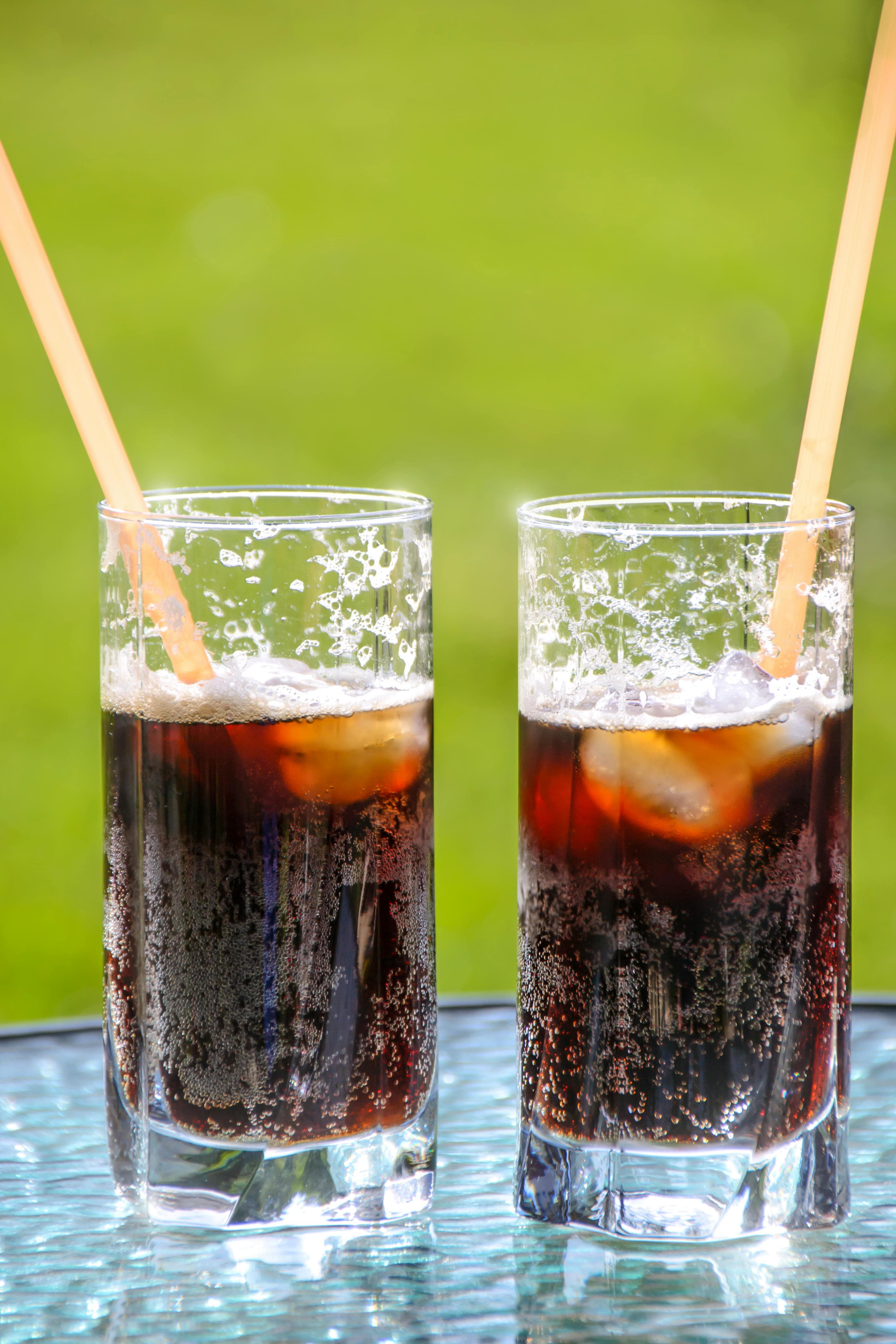 Two glasses with straws containing cola and ice.