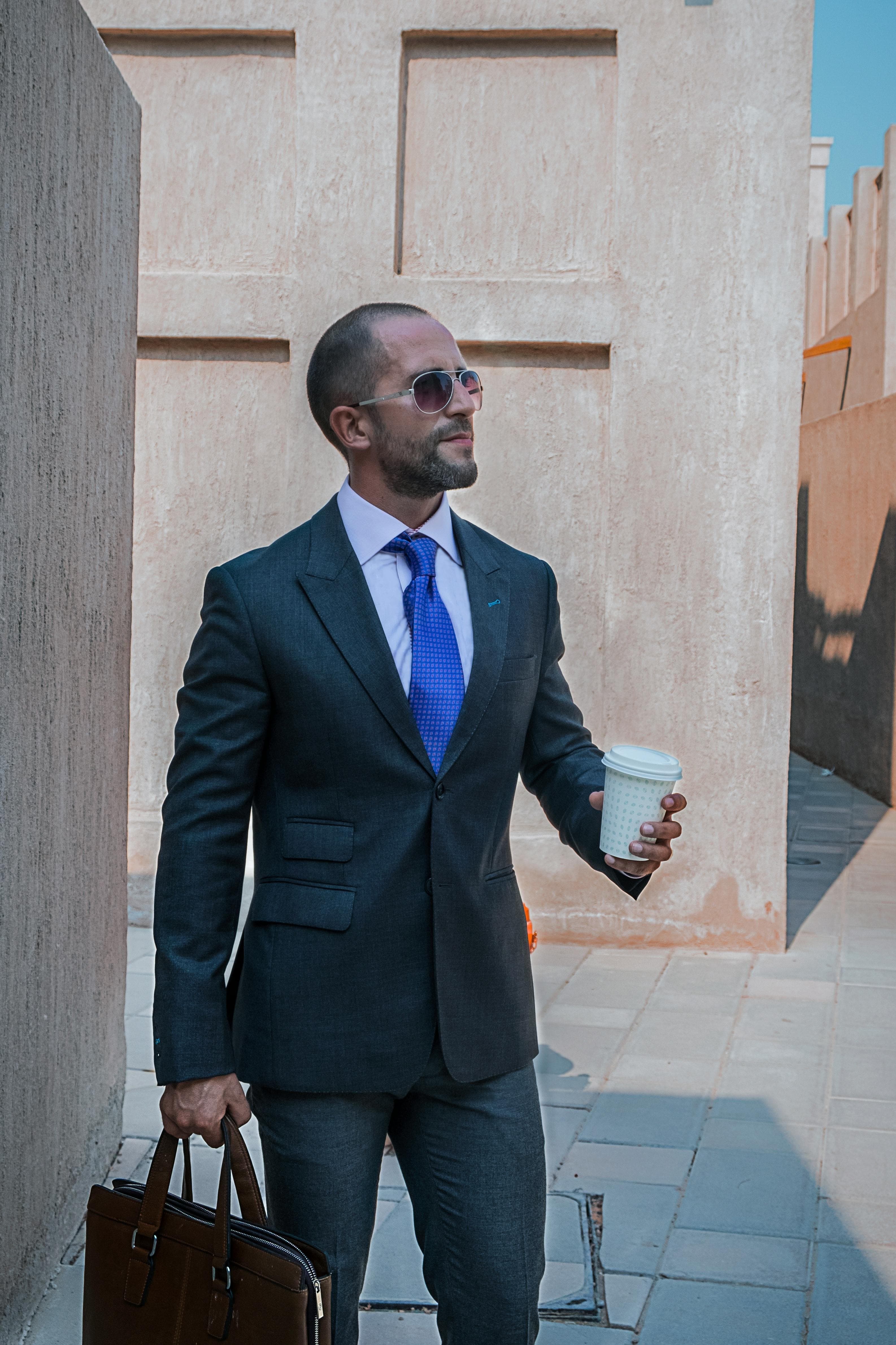 A man in sunglasses and a formal business suit holding coffee