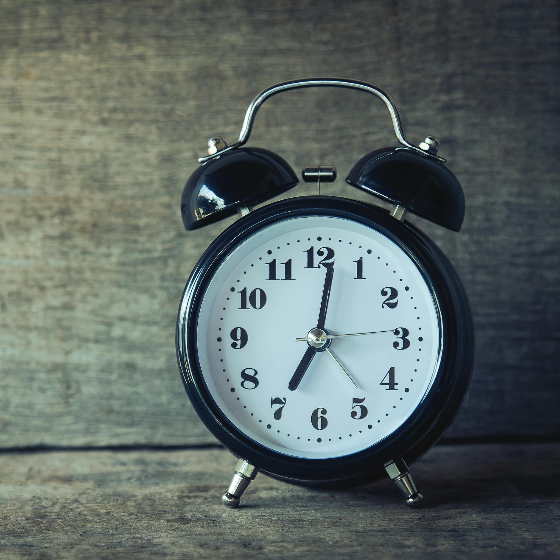 A photo of an old-fashioned black alarm clock reading 7:00.