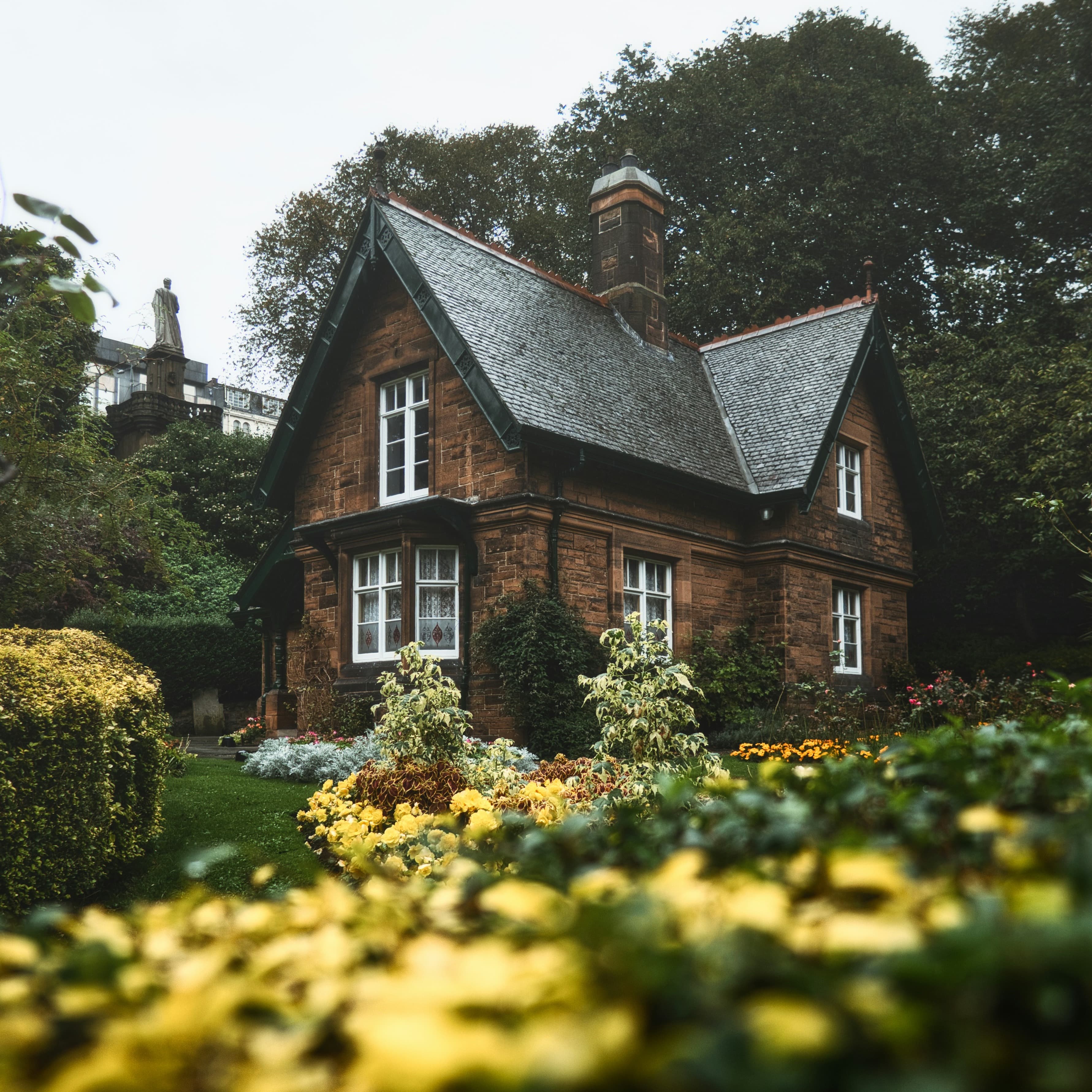 A photo of a brick house with a slate roof in a well-maintained garden on a rainy day.