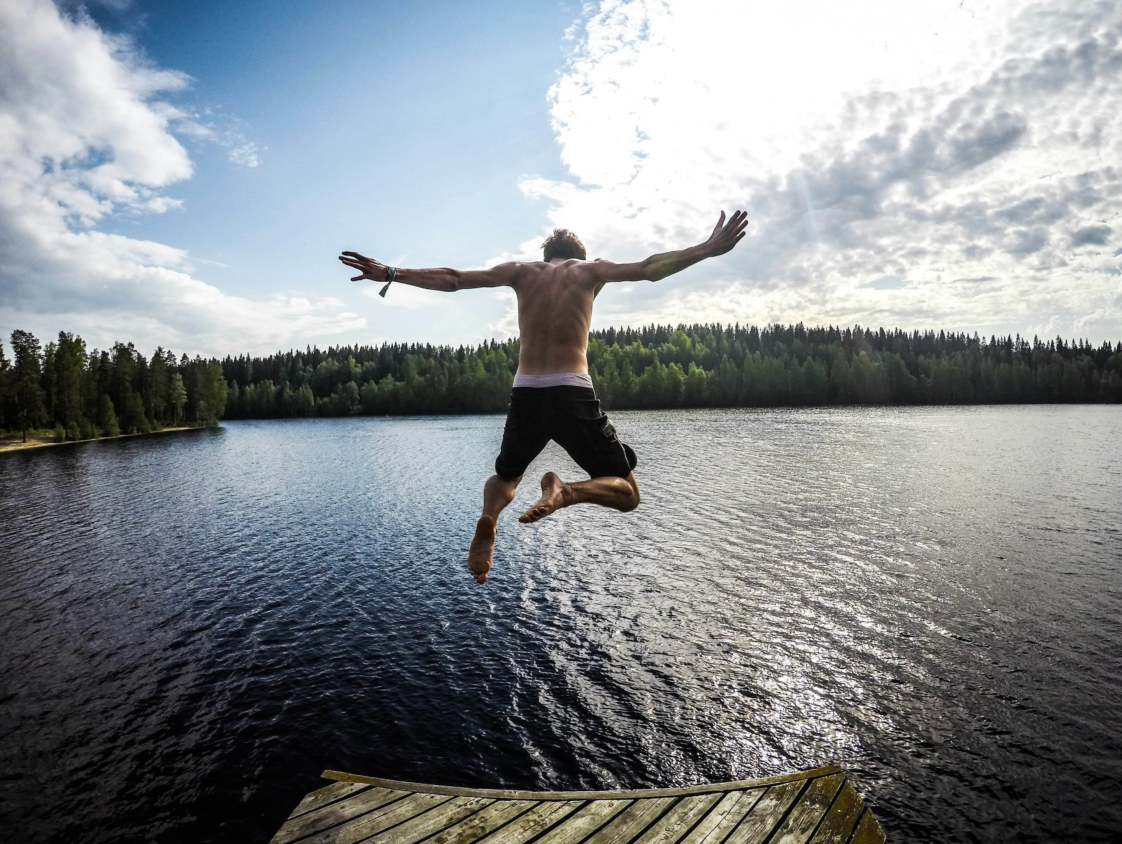 A photo taken from behind of a man jumping into a lake.
