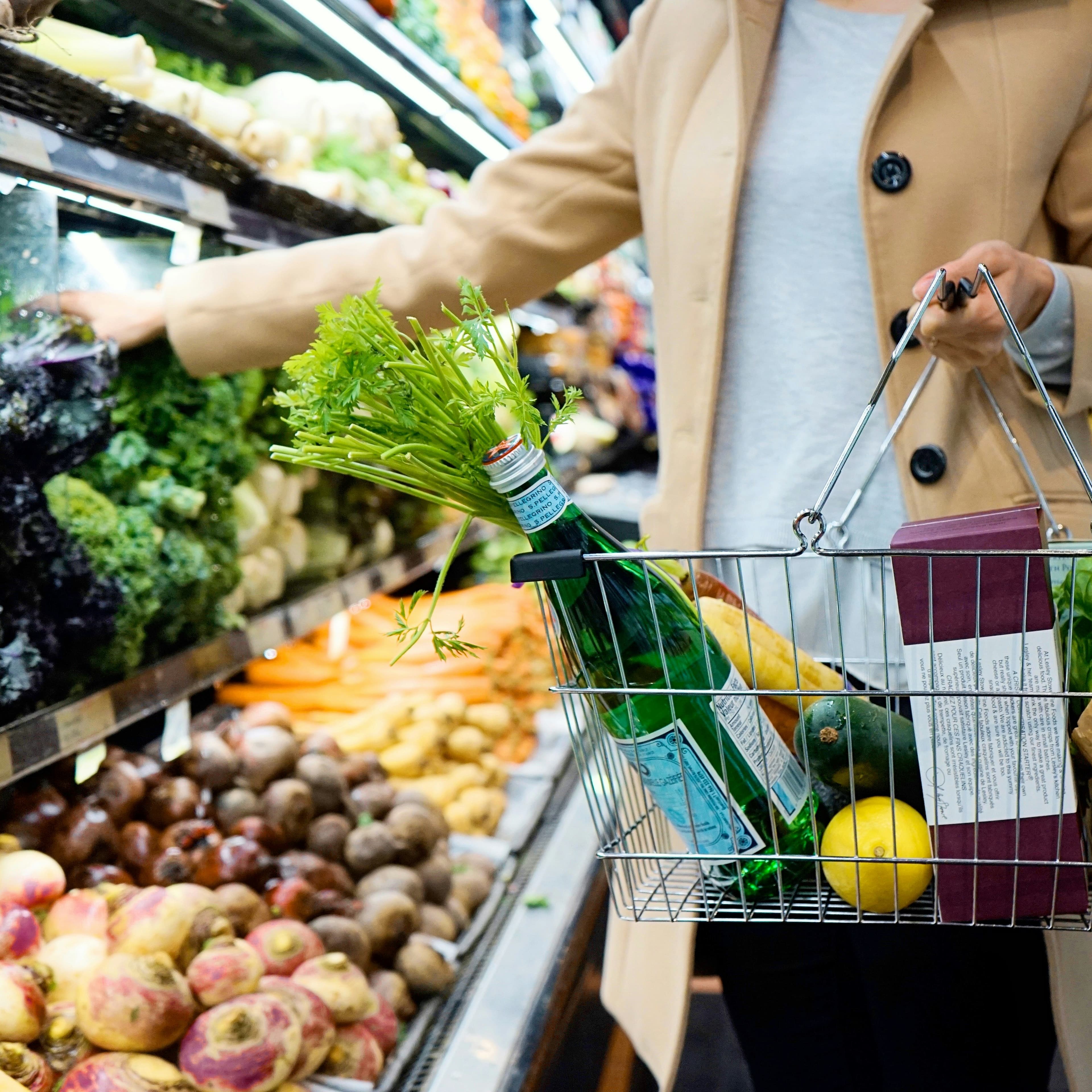 A photo of a woman gathering groceries into a basket.