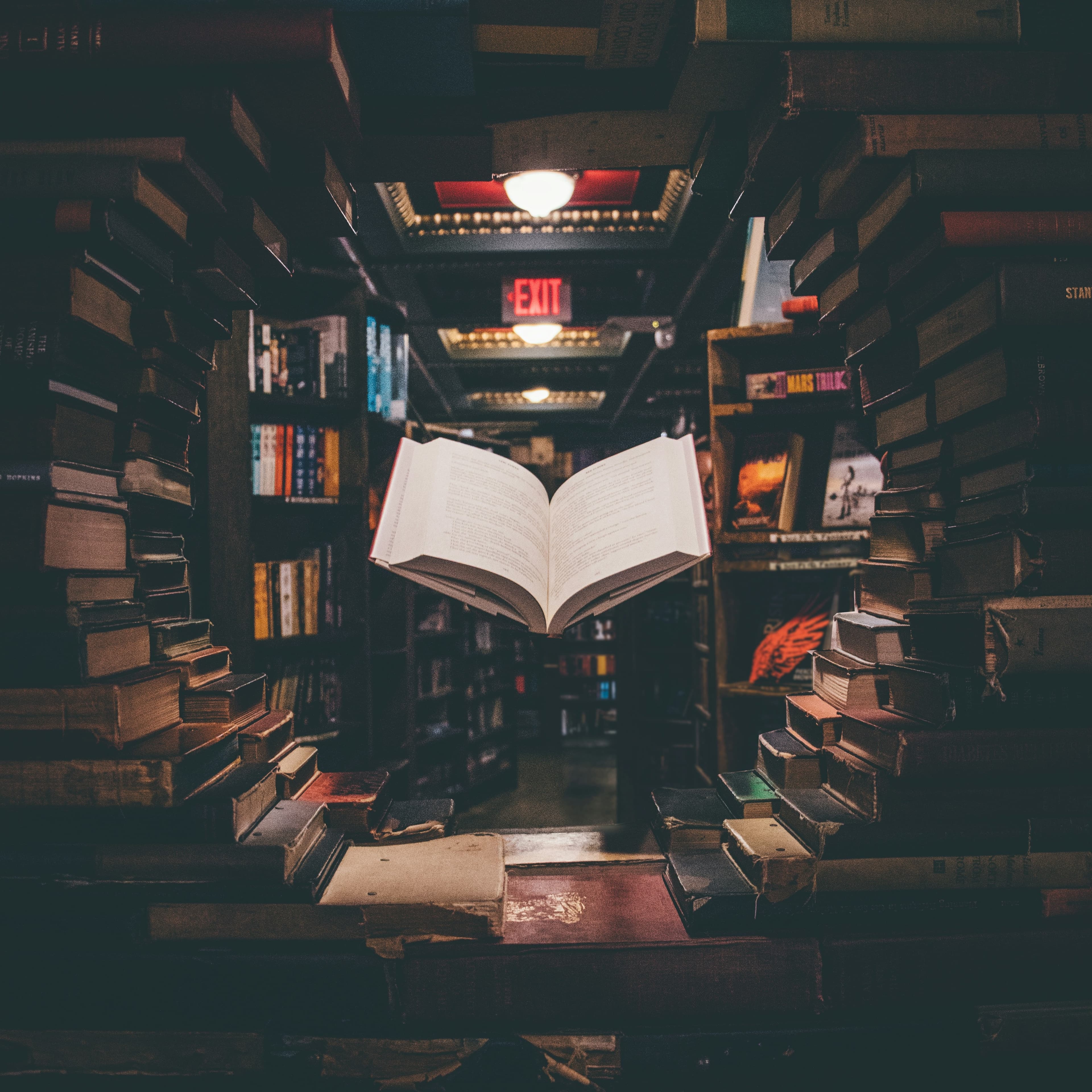 An open book floats magically in a circle of stacked books in the stacks of a library.