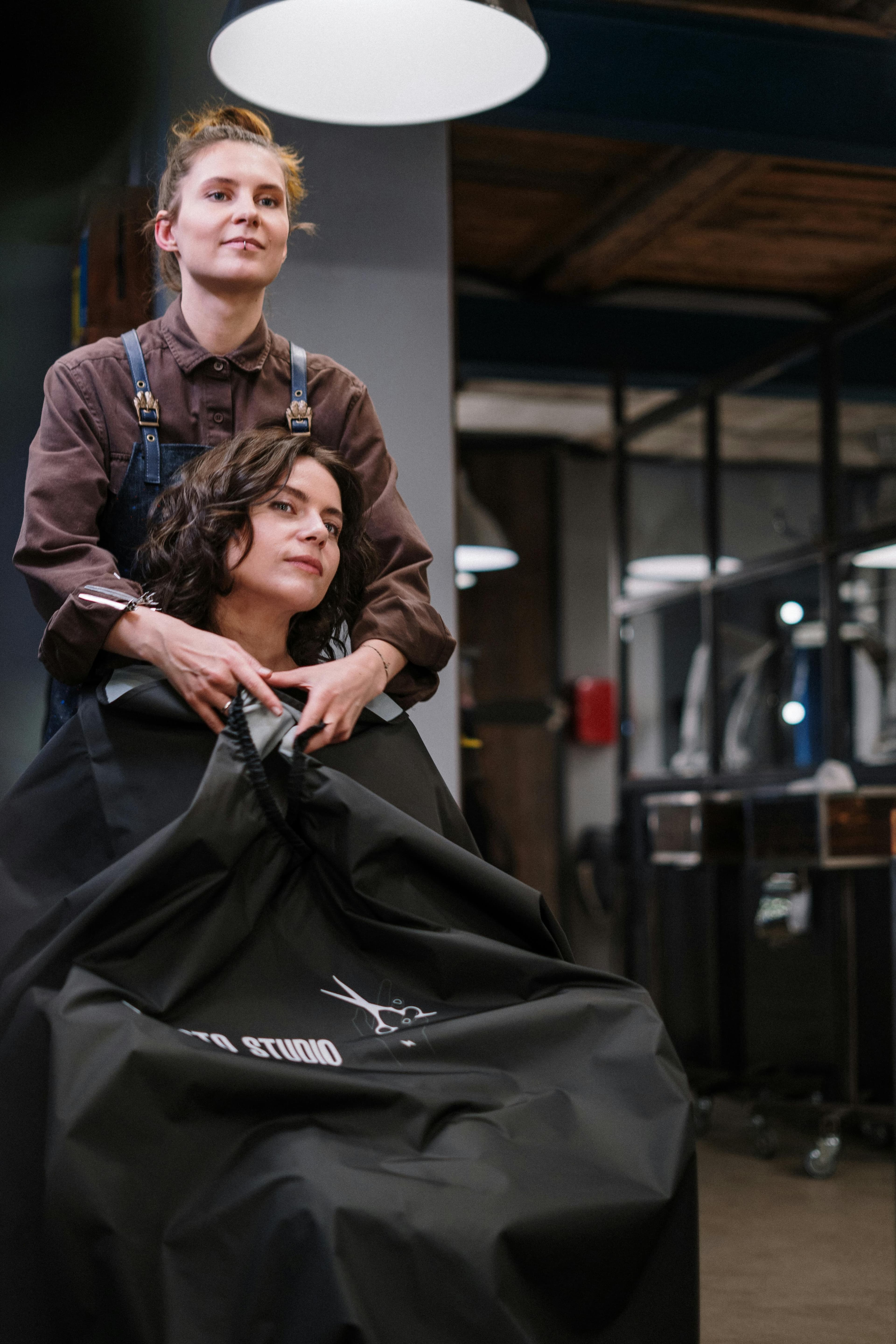 A woman is getting ready to have her hair cut at the salon. She and her stylist are looking at each other in the mirror.