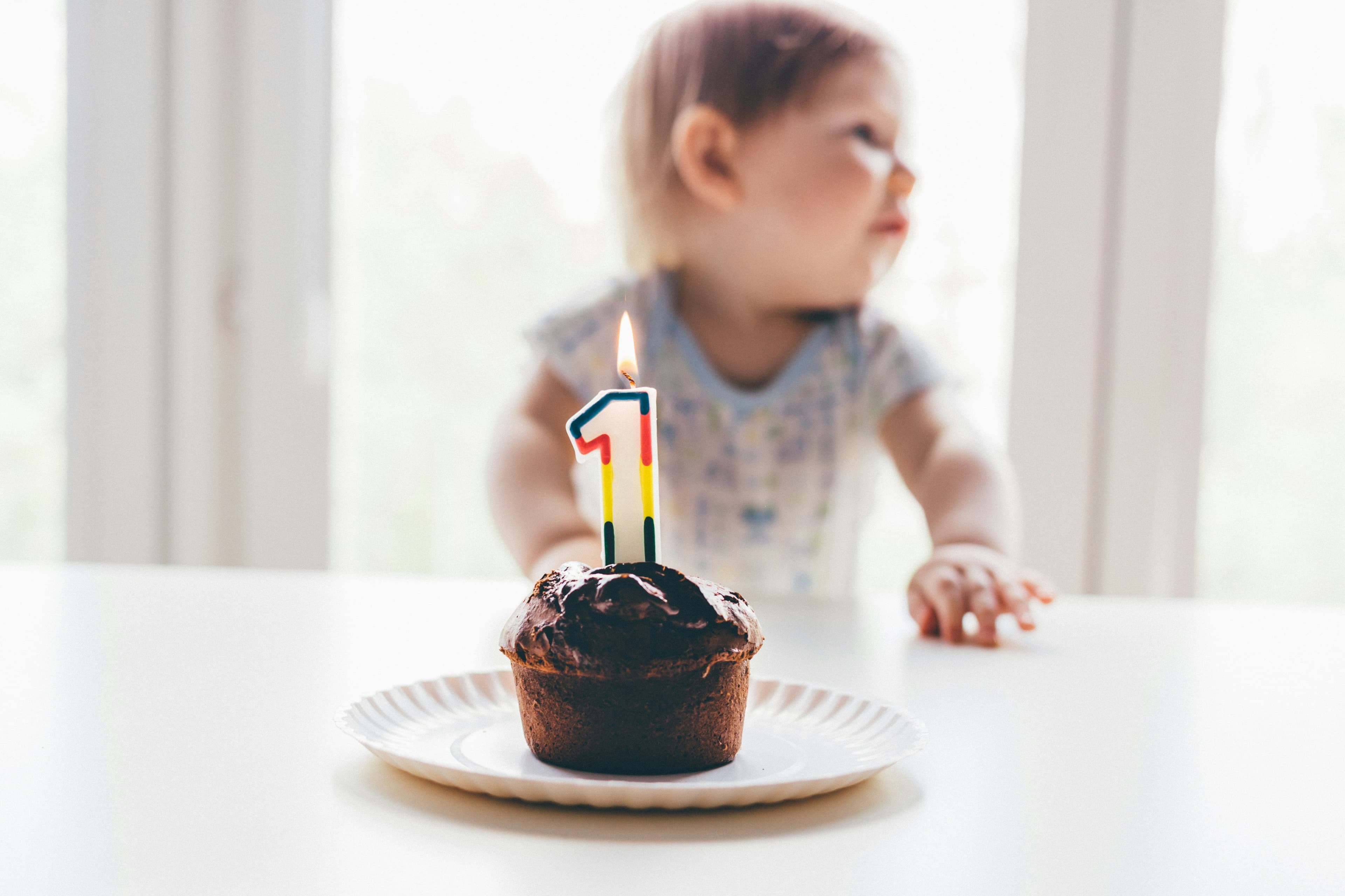 A photo of a toddler sitting in front of a cupcake with a birthday candle shaped like the number 1.
