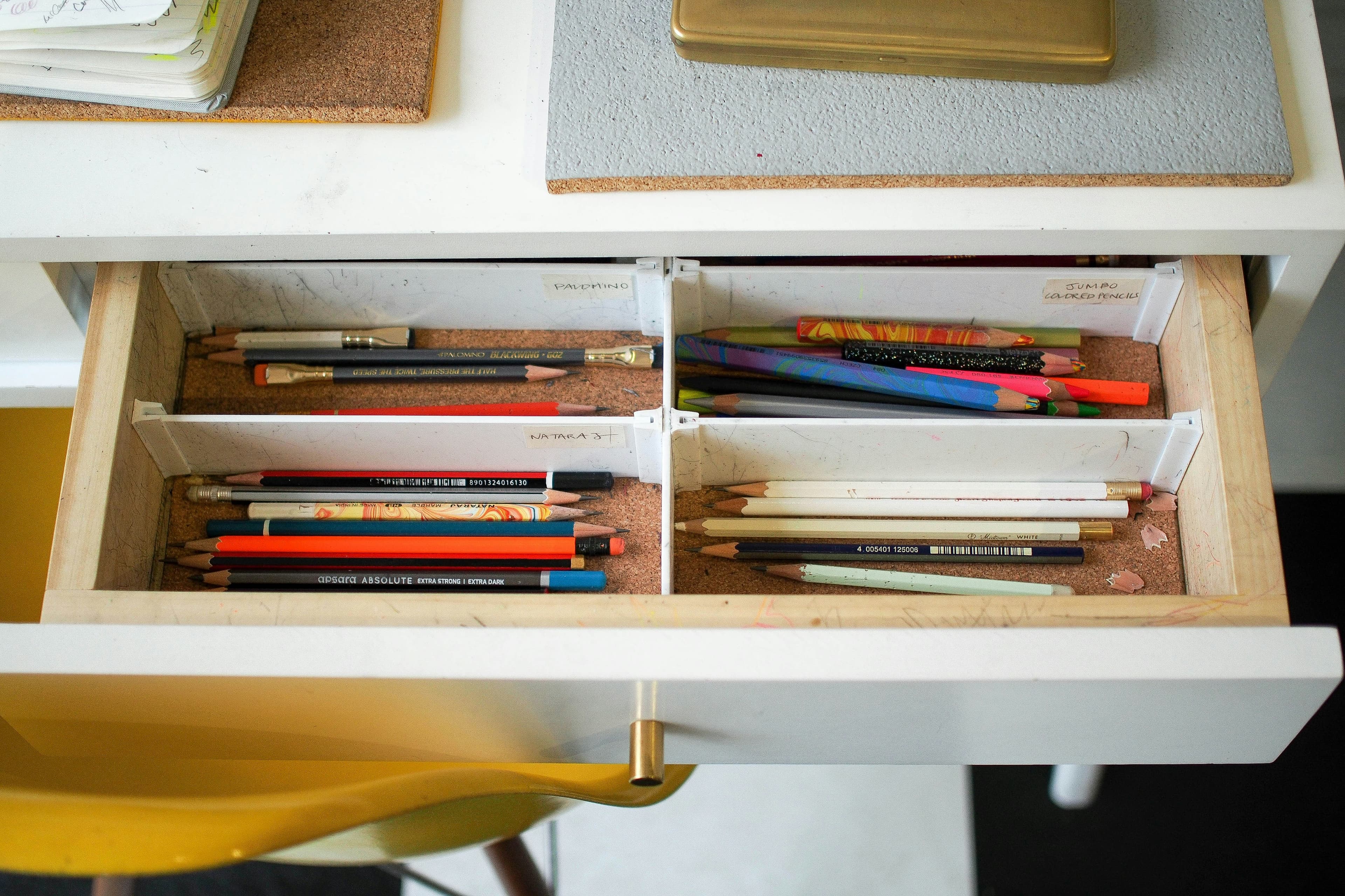 A photo of an open white desk drawer. It's divided into 4 sections, each holding pencils.