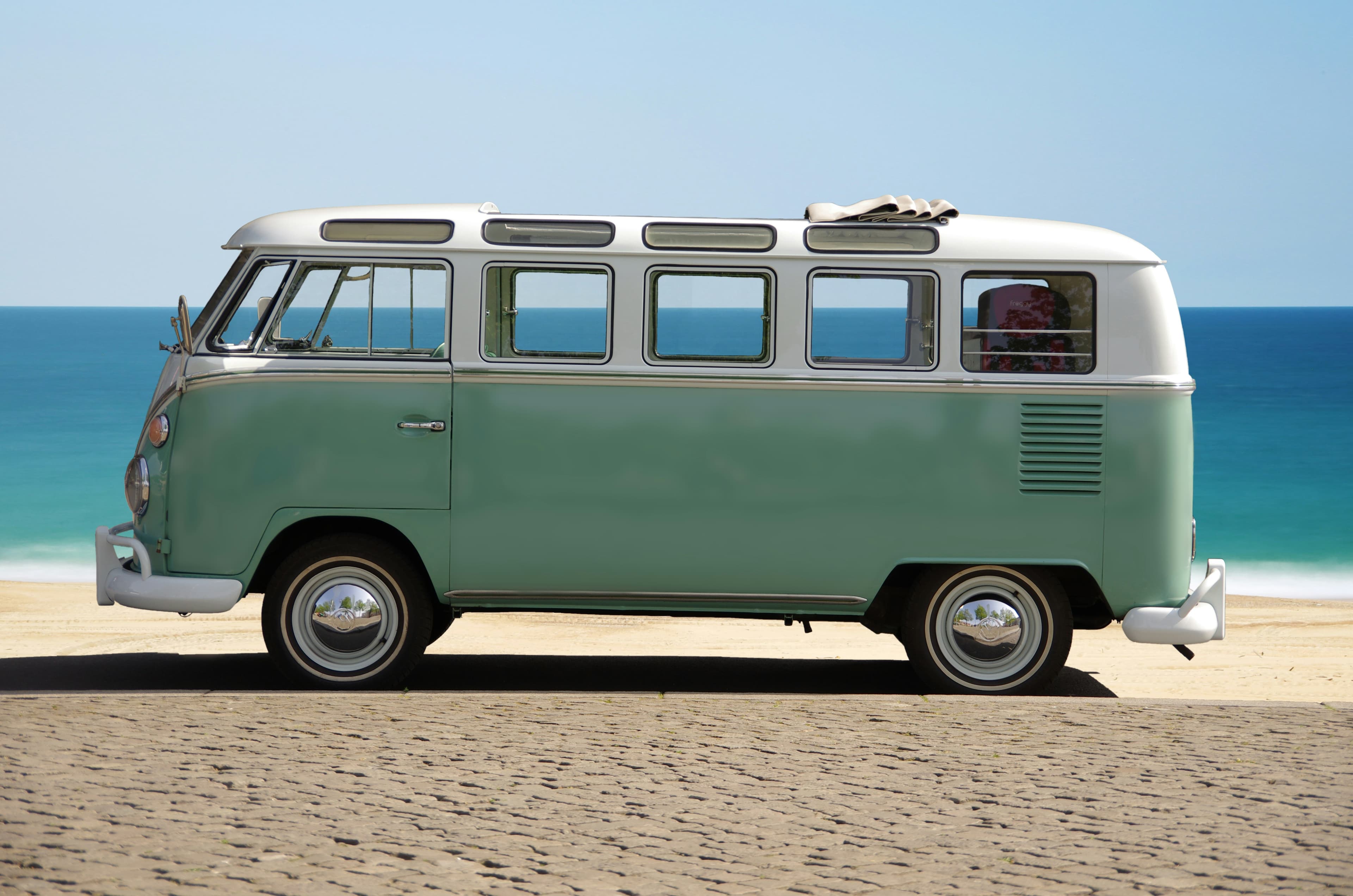 A mint green VW Bus on a beach in front of the blue water.