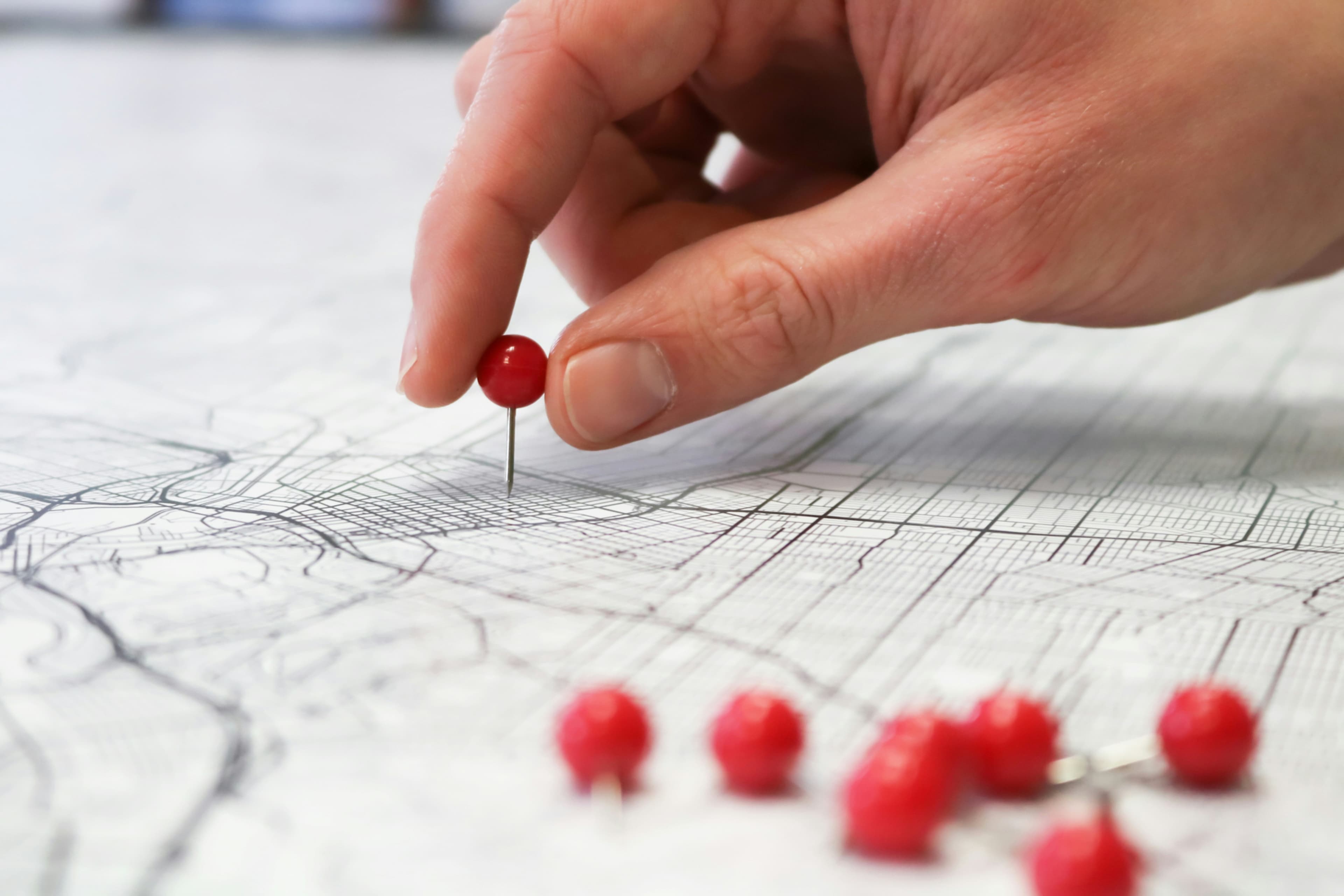 A photo of a white hand pushing a red pin into a map of streets.