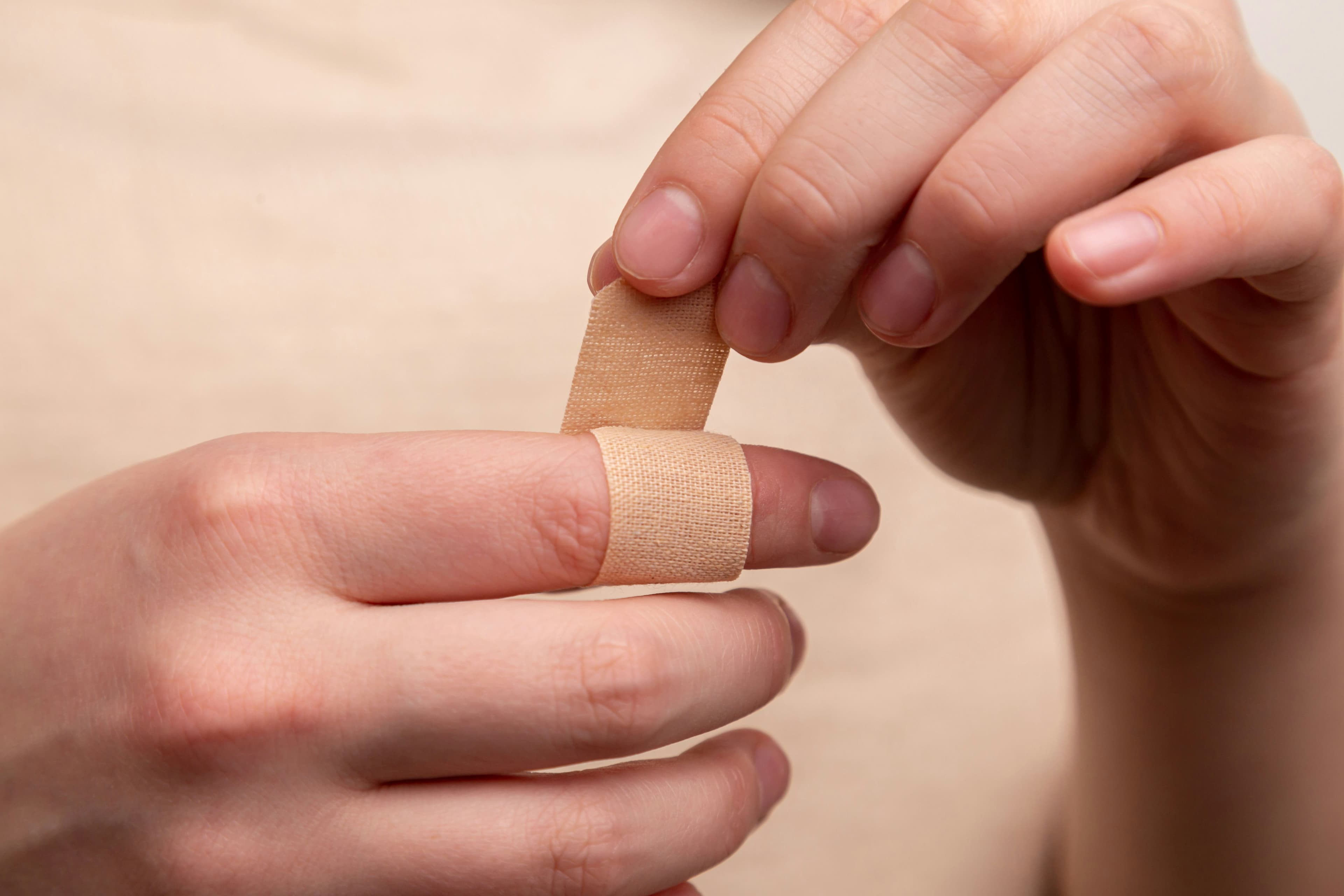 A photo of a someone putting a bandage around the knuckle of their pointer finger.