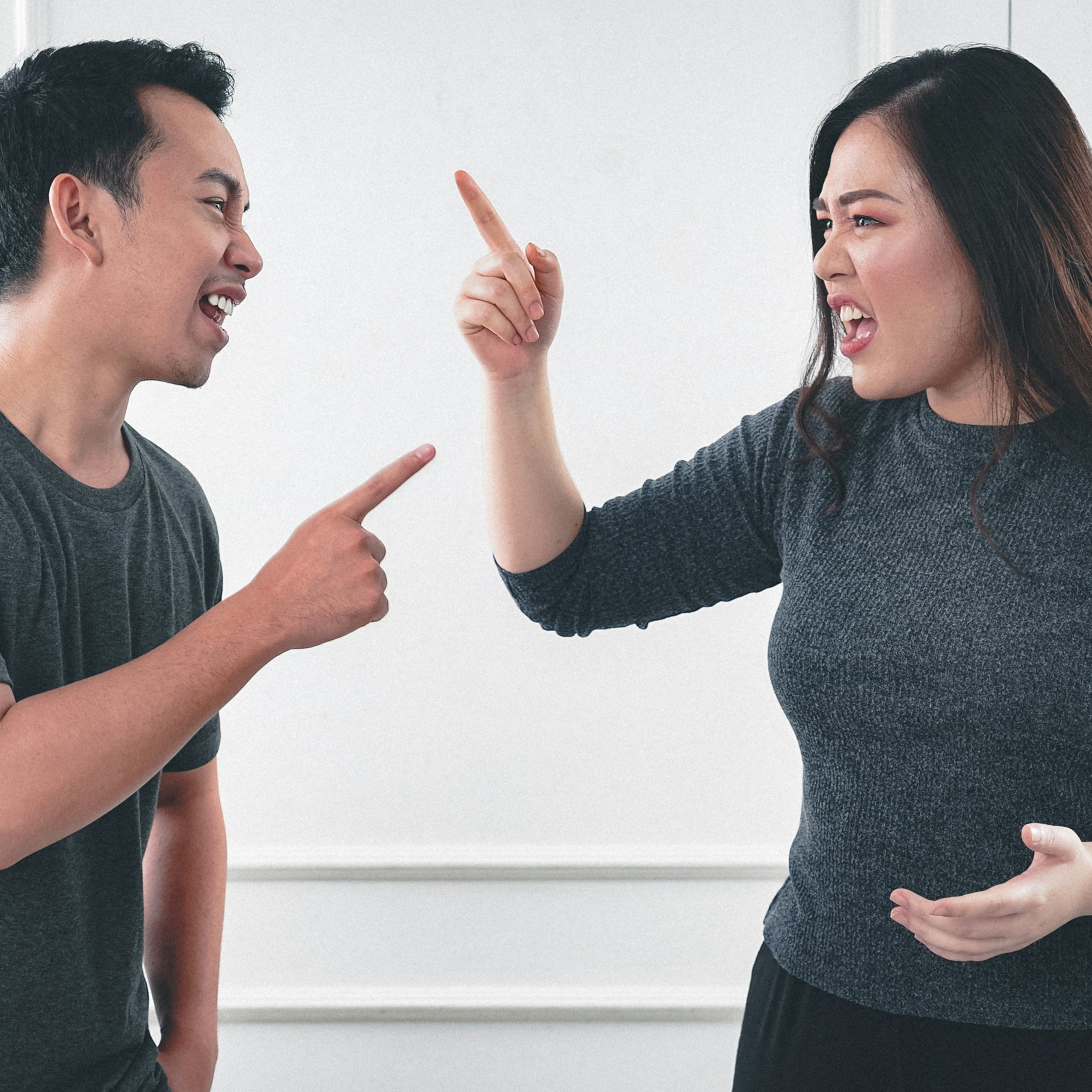 A photo of a man and woman arguing. They are pointing fingers at each other and both seem to be speaking at the same time.