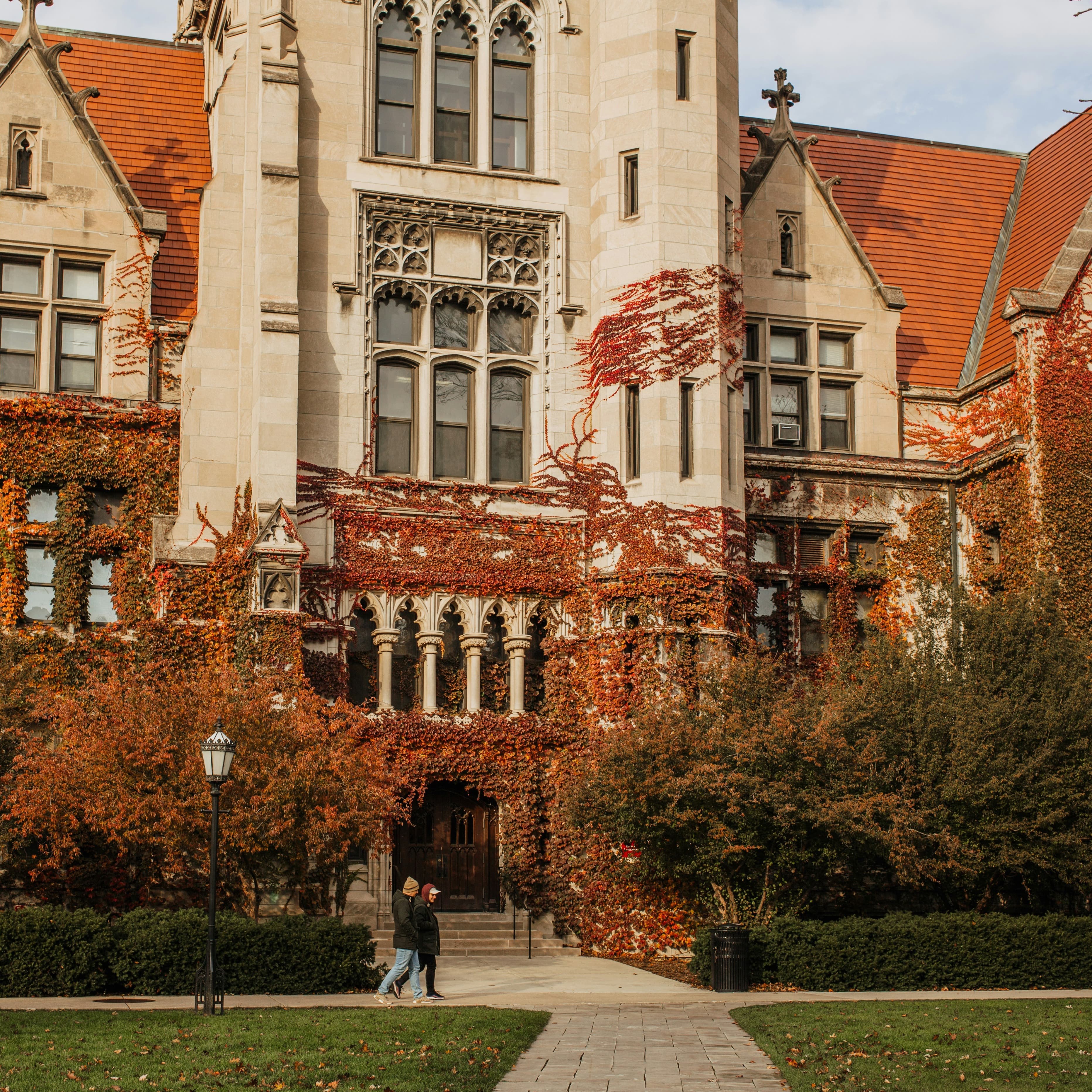 A photo of a a gothic-style university building in the fall. Red ivy climbs up the facade.