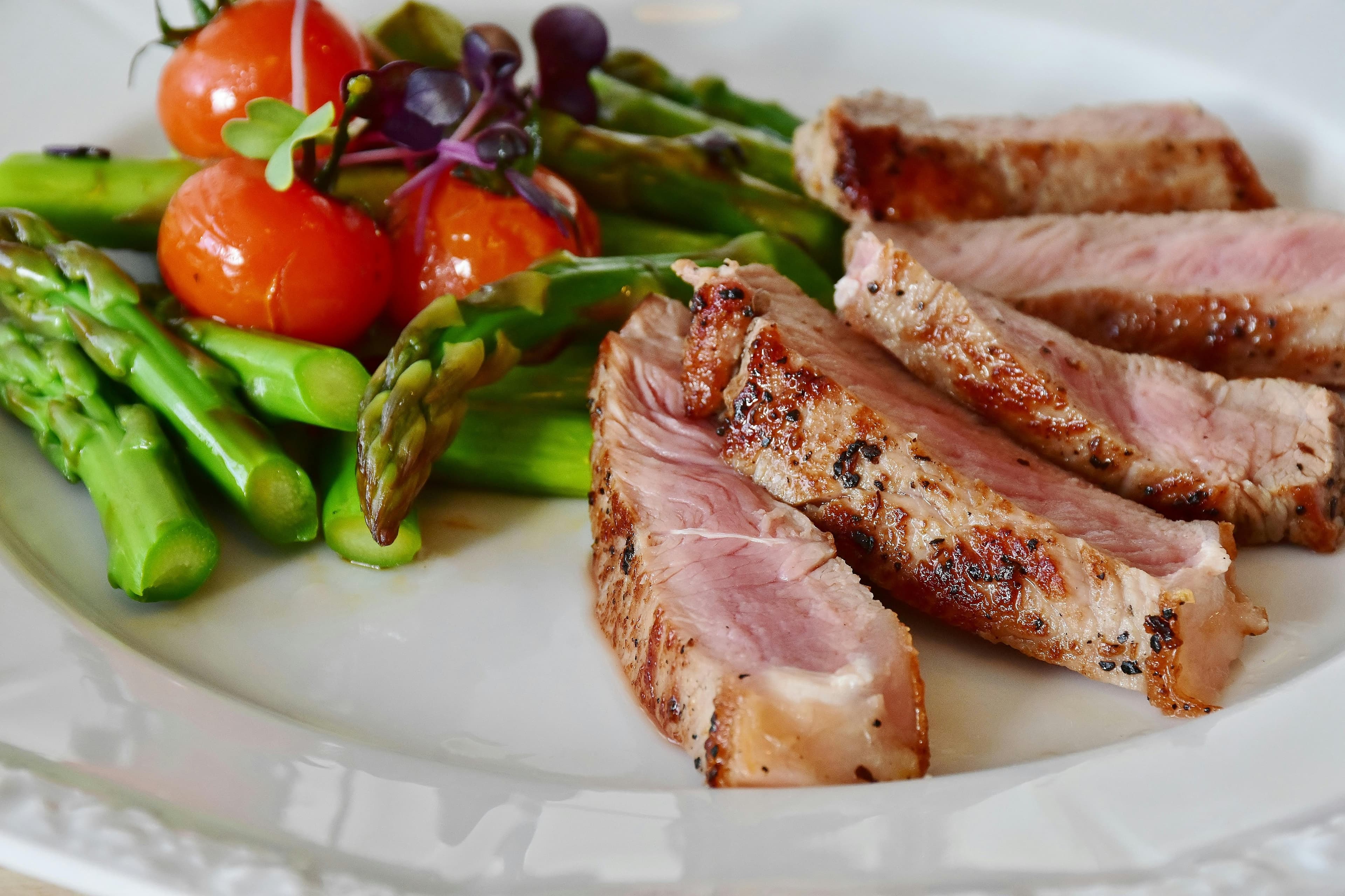 A plate contains five slices of steak along with some mixed vegetables.