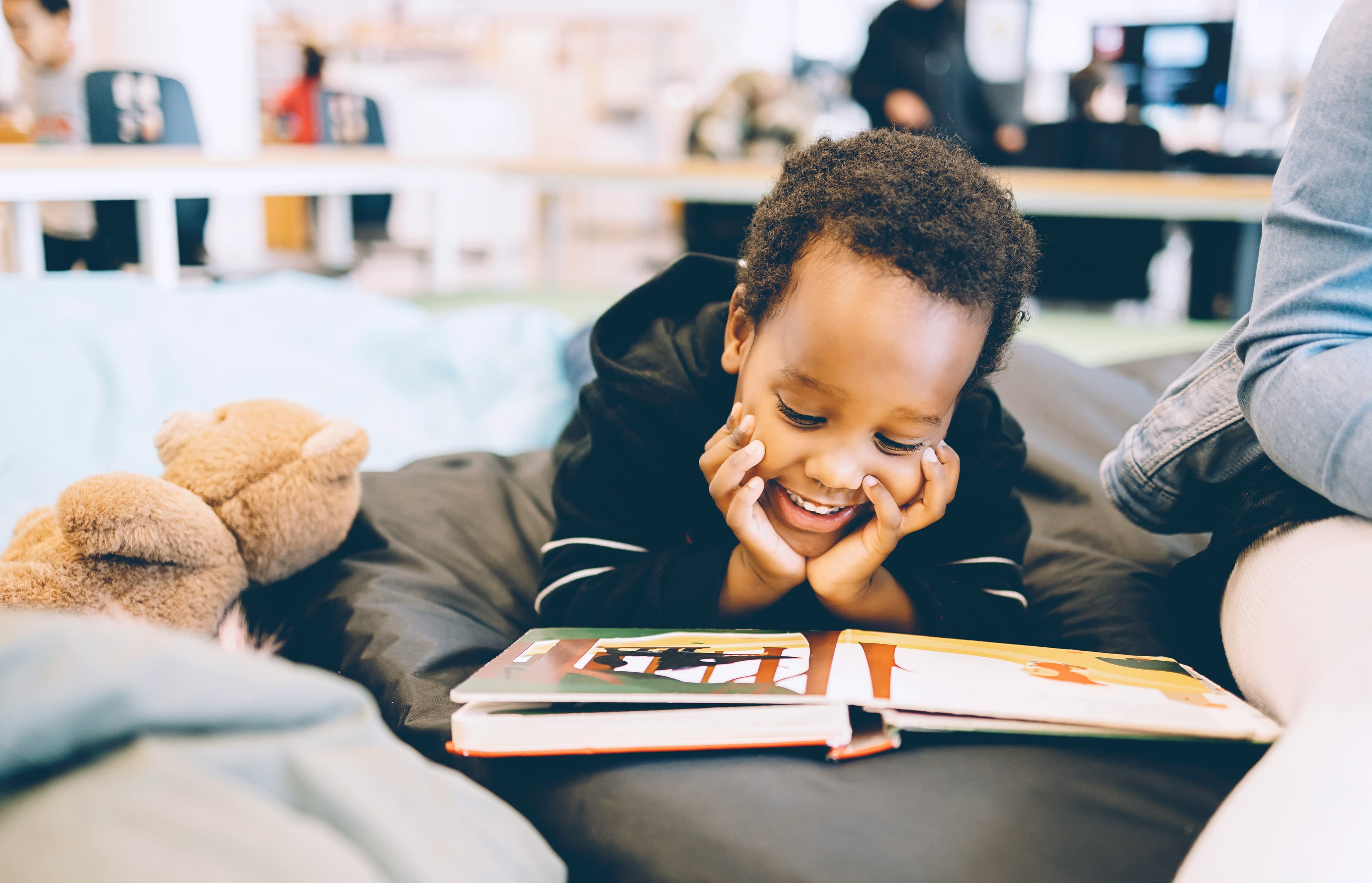 A photo of a little boy lying on his stomach and reading a book.